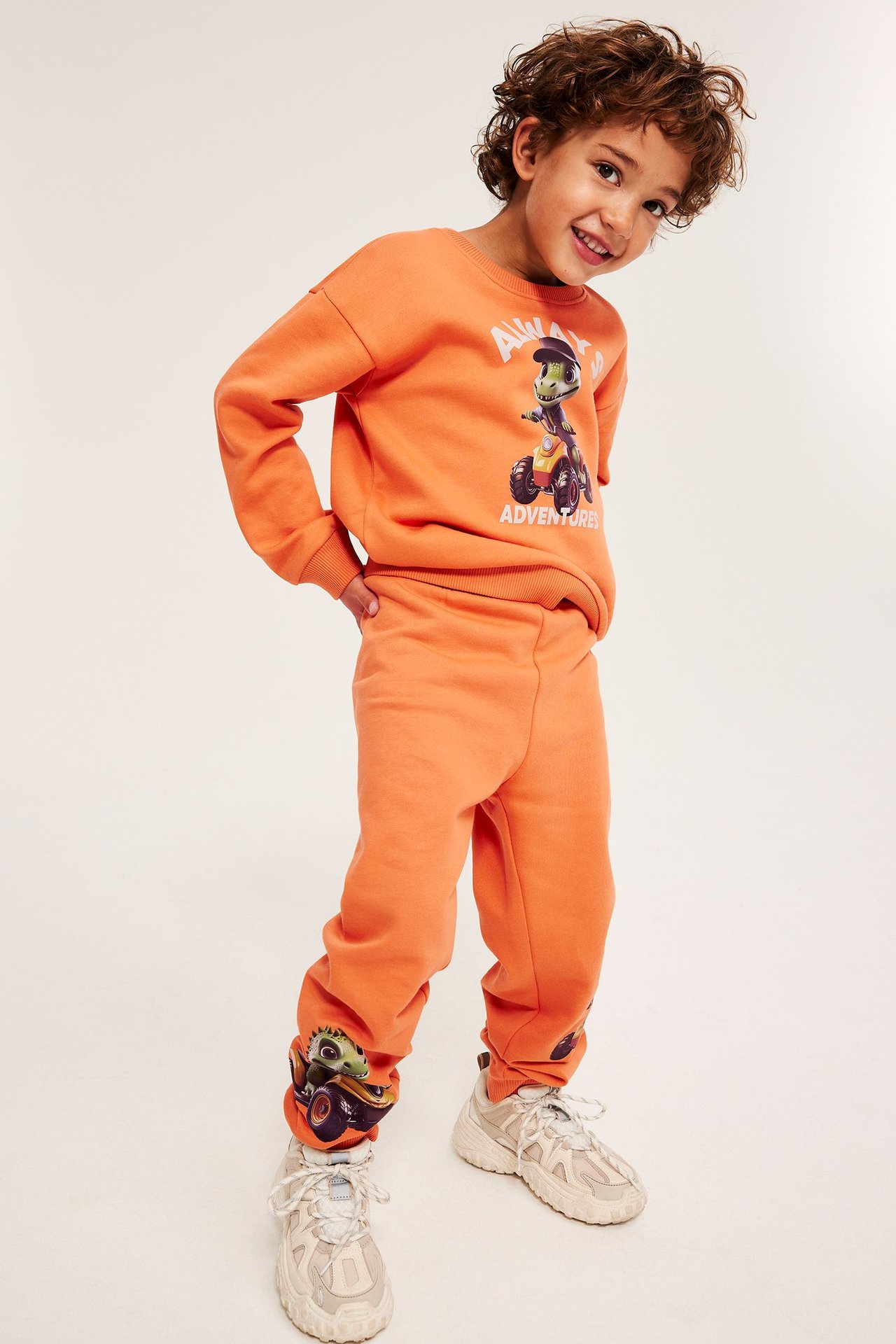 Frontutsikt: Barn i oransje joggebukser med dinoprint, matchende genser og lyse joggesko.