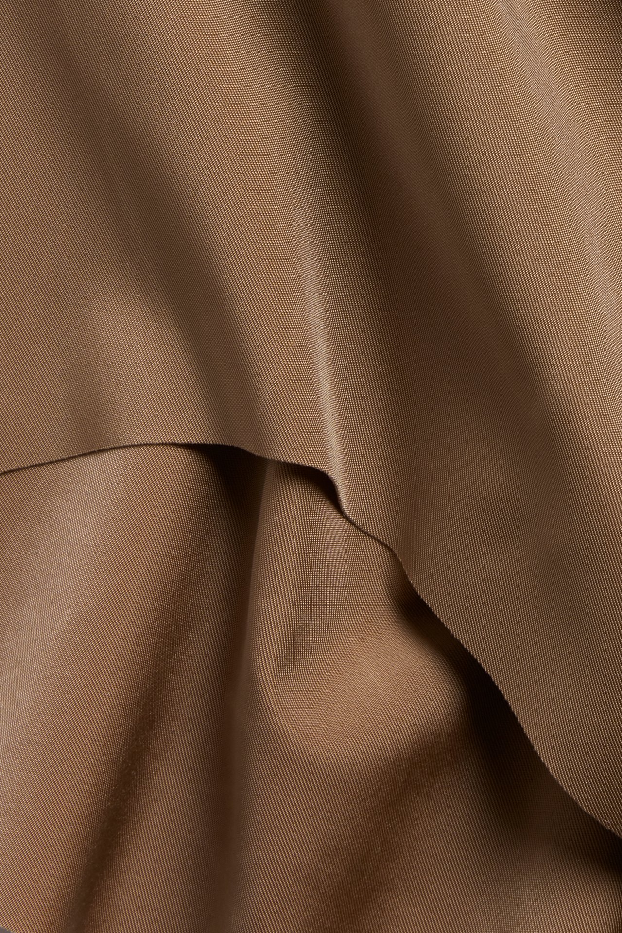 Zbliżenie miękkiej brązowej tkaniny mikrofibrowej z ukośnym prążkowaniem i delikatnymi fałdami.