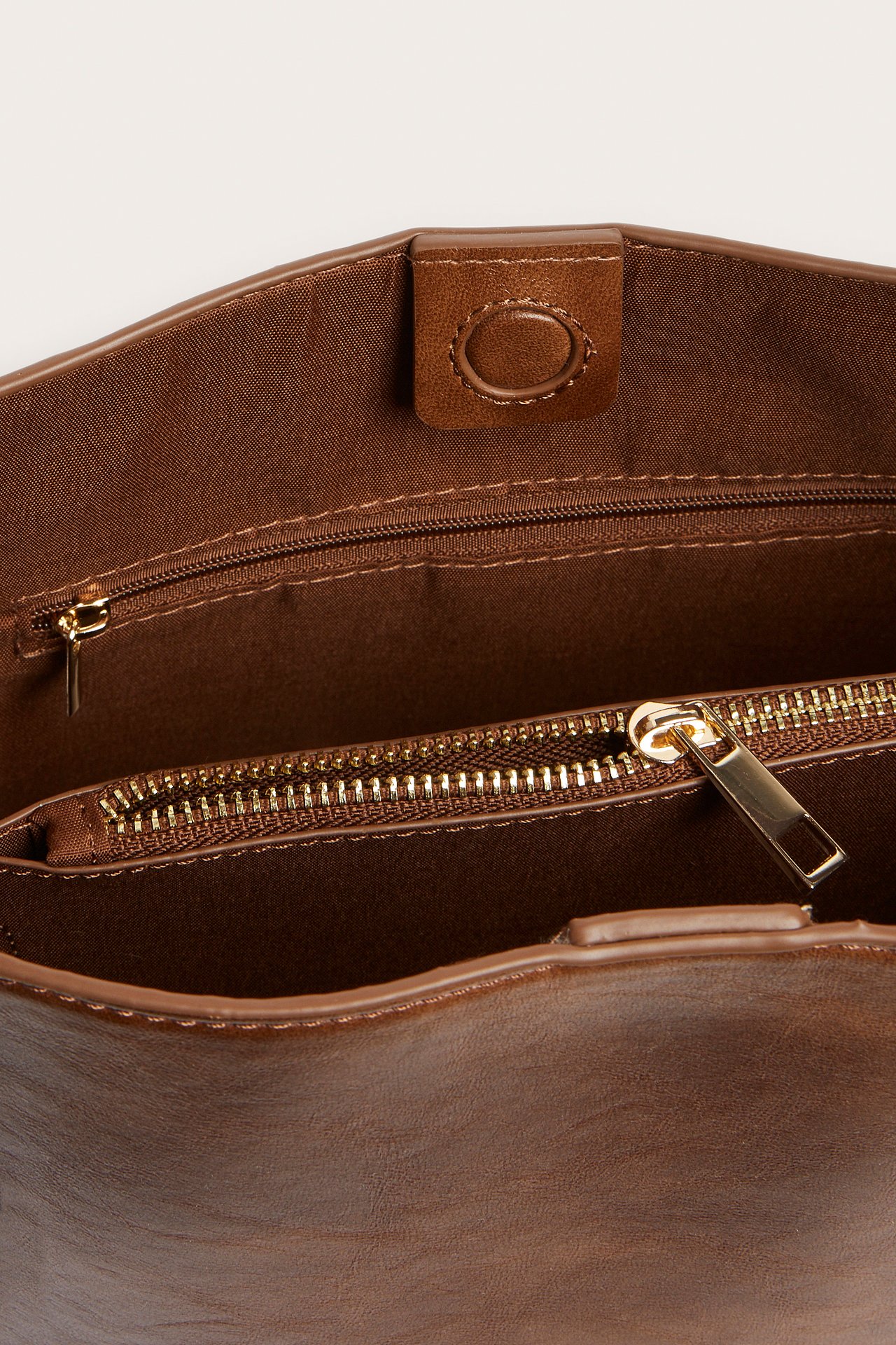 Lähikuva avoimesta ruskeasta käsilaukusta, jossa magneettikiinnitys ja vetoketjullinen sisätasku.