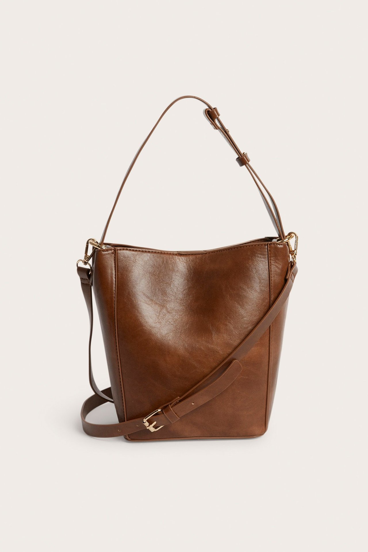 Frontvisning av en brun håndveske med justerbar skulderrem og en lengre cross-body stropp.