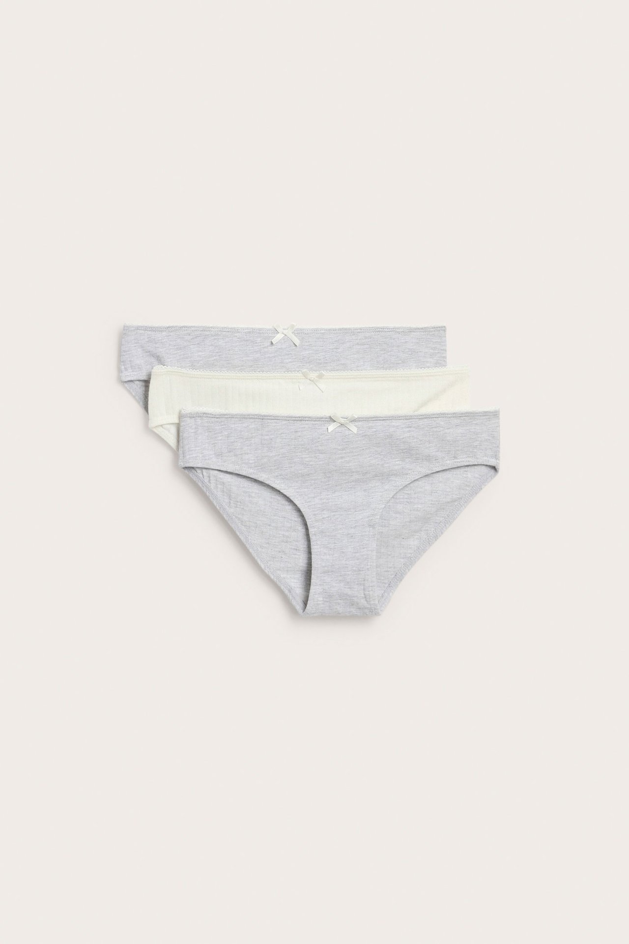 Trzy prążkowane majtki: dwa jasnoszare, jedne kremowe, z wykończeniem picot i małymi kokardkami z przodu.