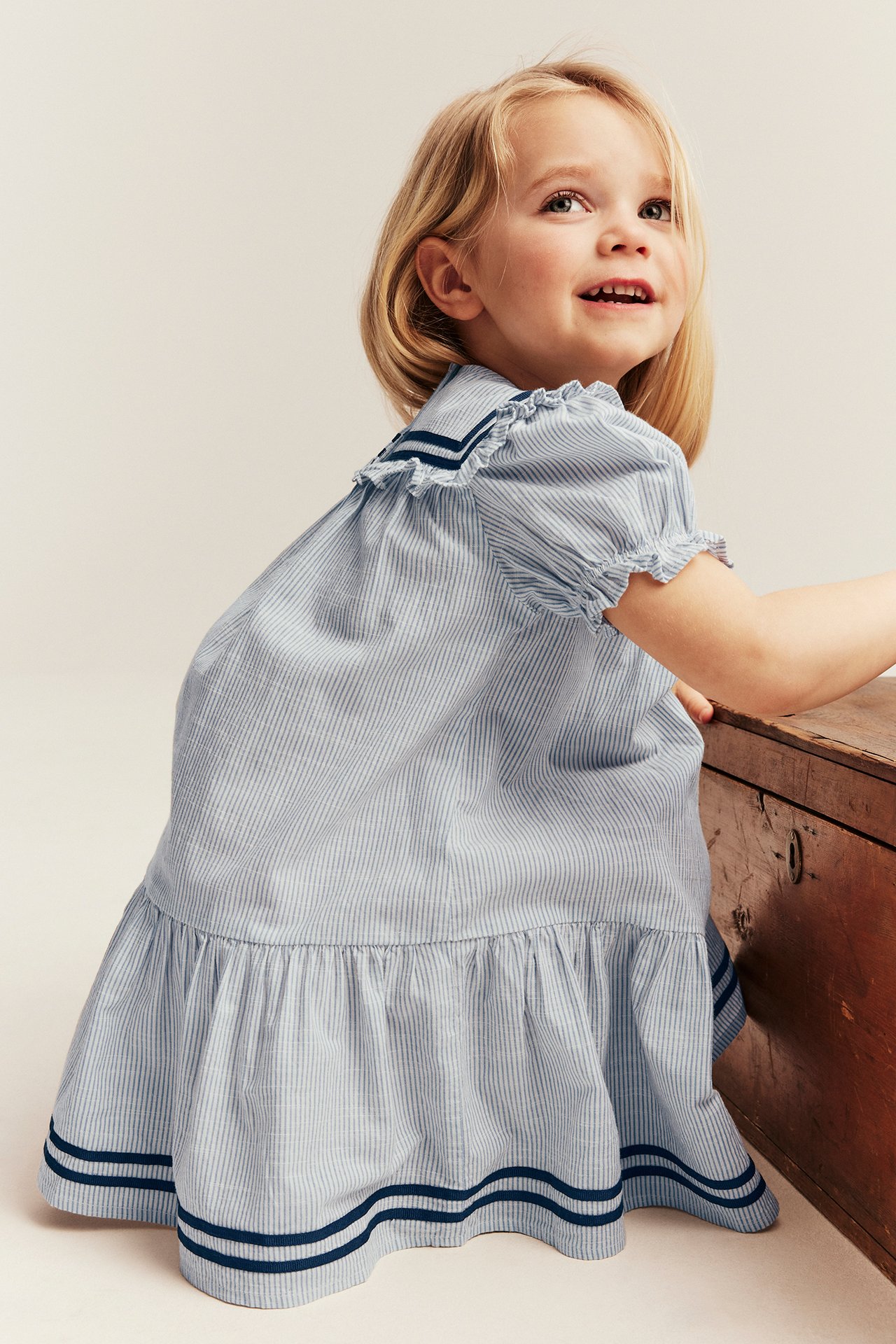 Barn i en lys blåstripet bomullskjole med sjømannskrage, puffermer og blå bånd.