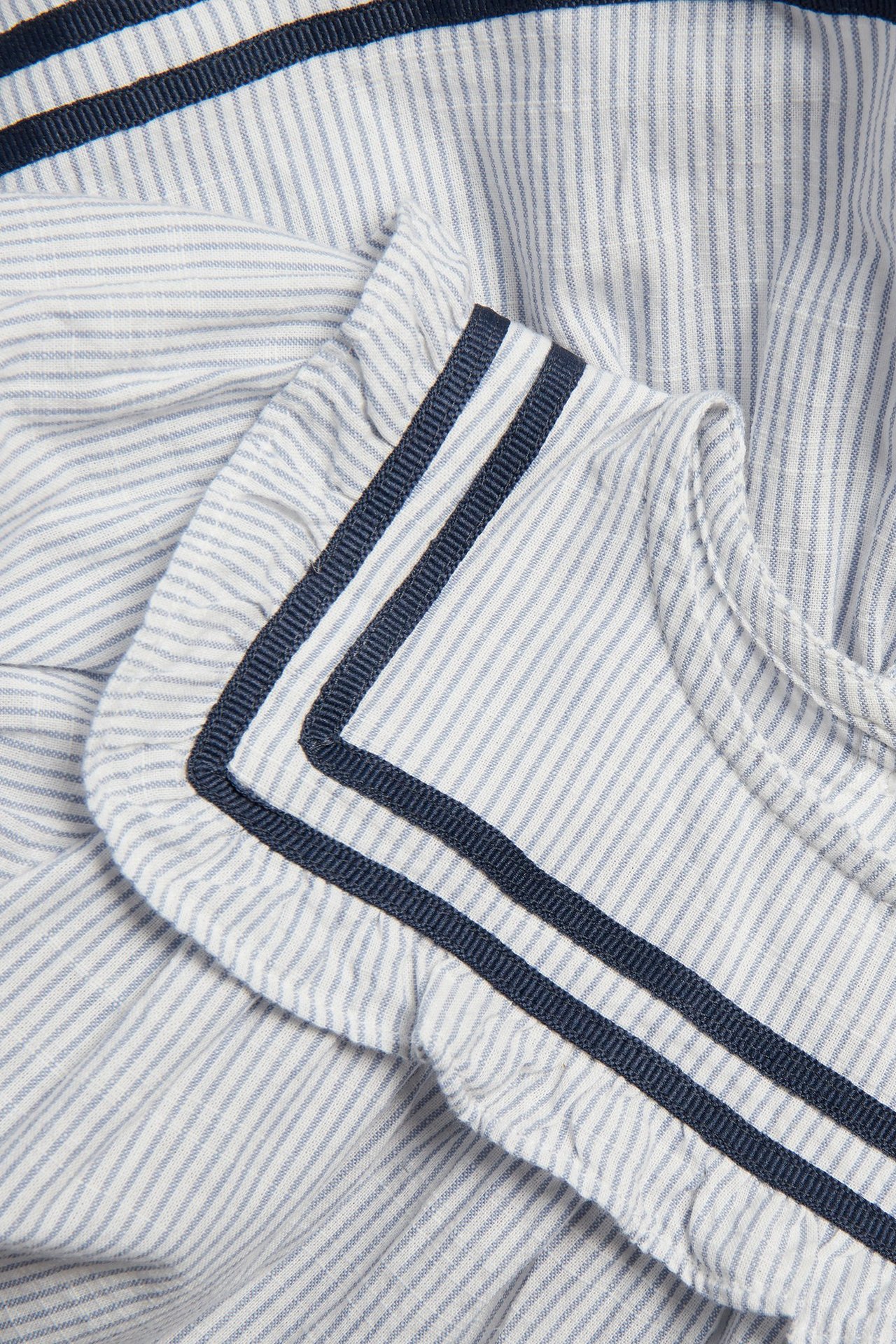 Zbliżenie na niebiesko-białą sukienkę w paski, z falbaniastym karczkiem i granatową tasiemką.