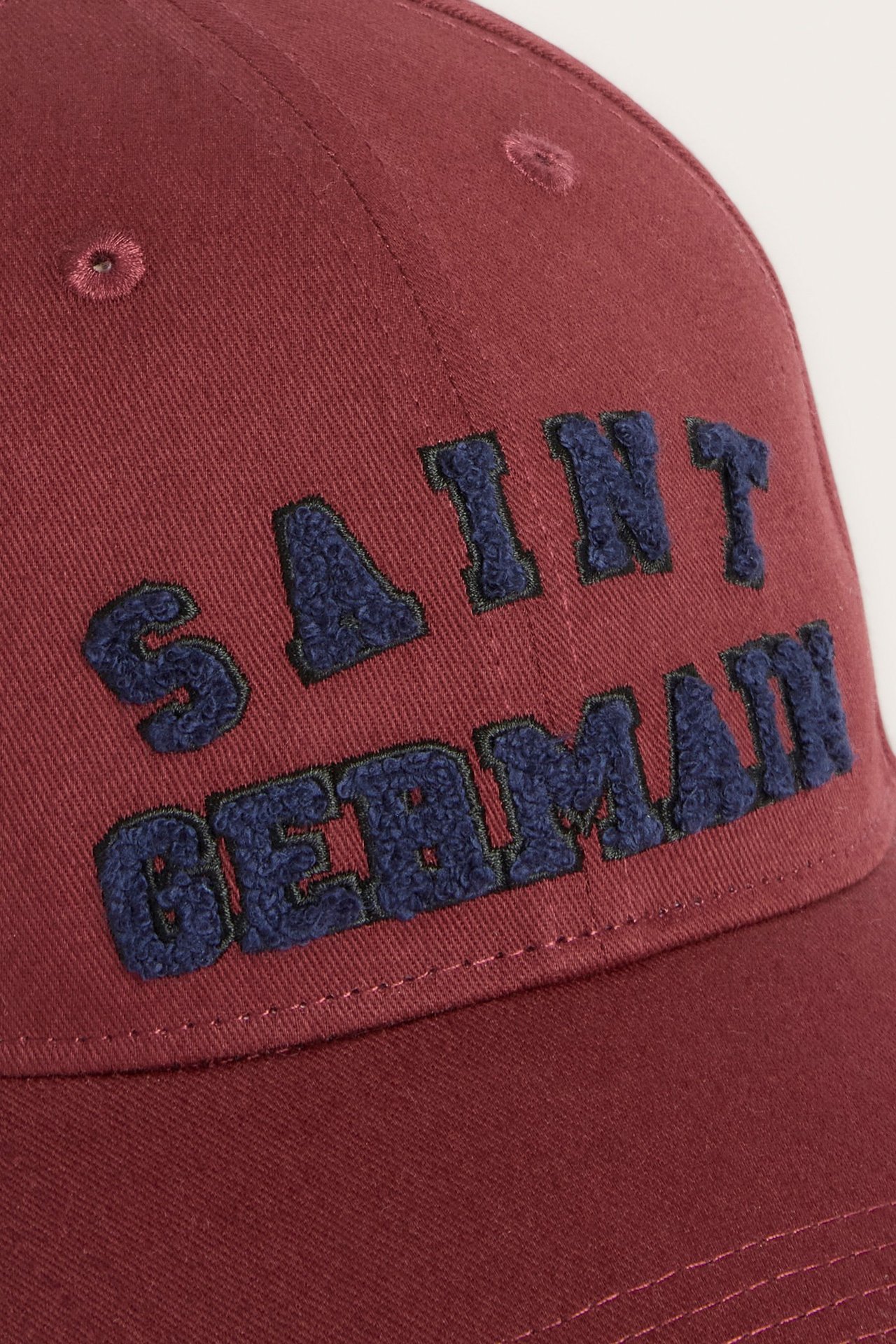 Lähikuva punaisesta puuvillaisesta lippiksestä, jossa on sininen brodeerattu teksti "SAINT GERMAIN".