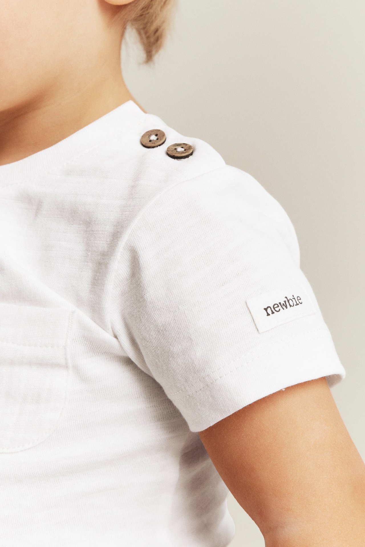 Nærbilde av en babys offwhite kortermet body i slubtrikot med treknapper på skulderen og brystlomme.