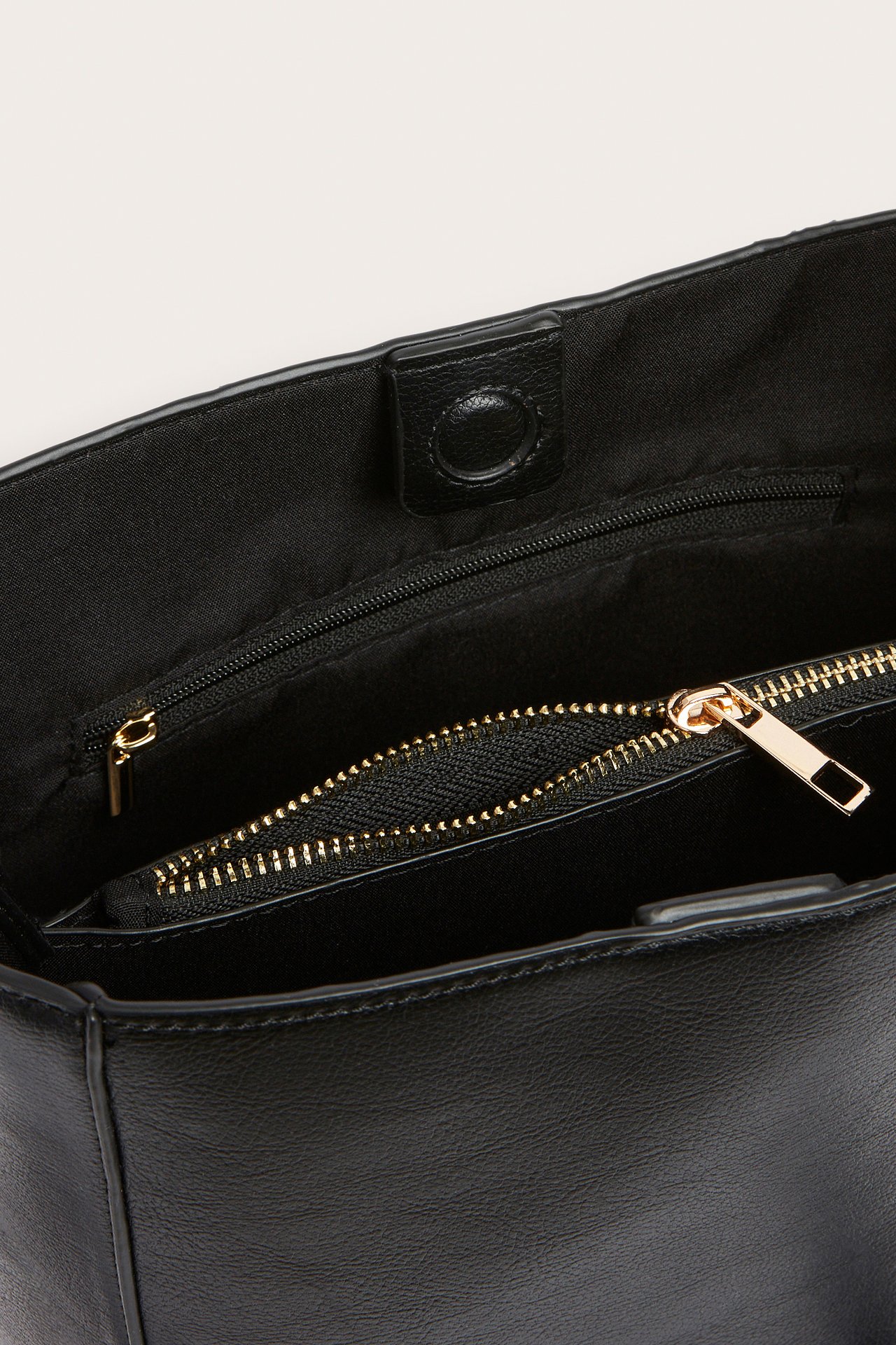 Lähikuva avoimesta mustasta käsilaukusta, jossa magneettisuljenta ja sisällä kultavetoketjullinen tasku.