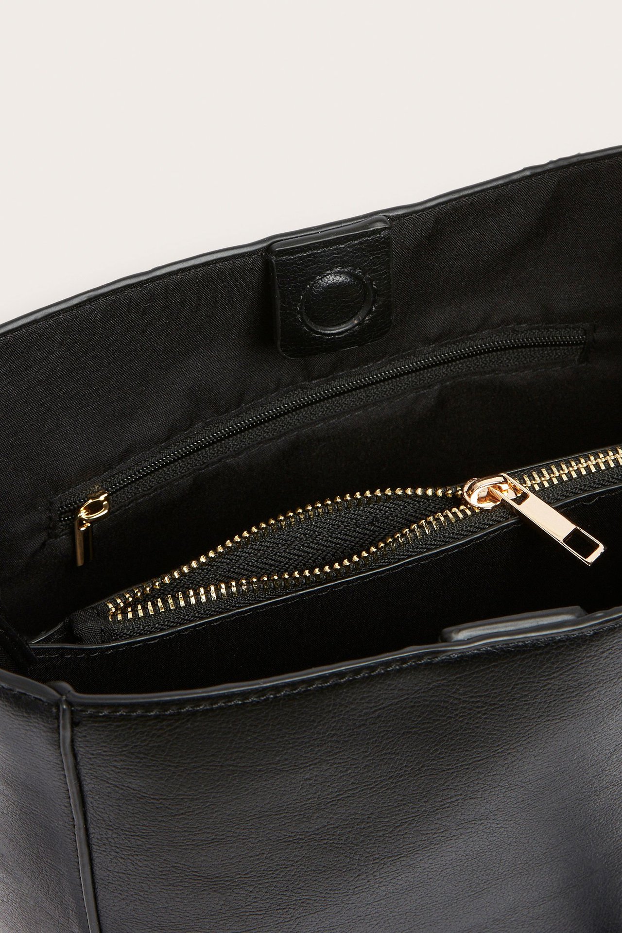 Nærbilde av åpen svart håndveske med magnetlås, som viser en innerlomme med gullglidelås og fôr.