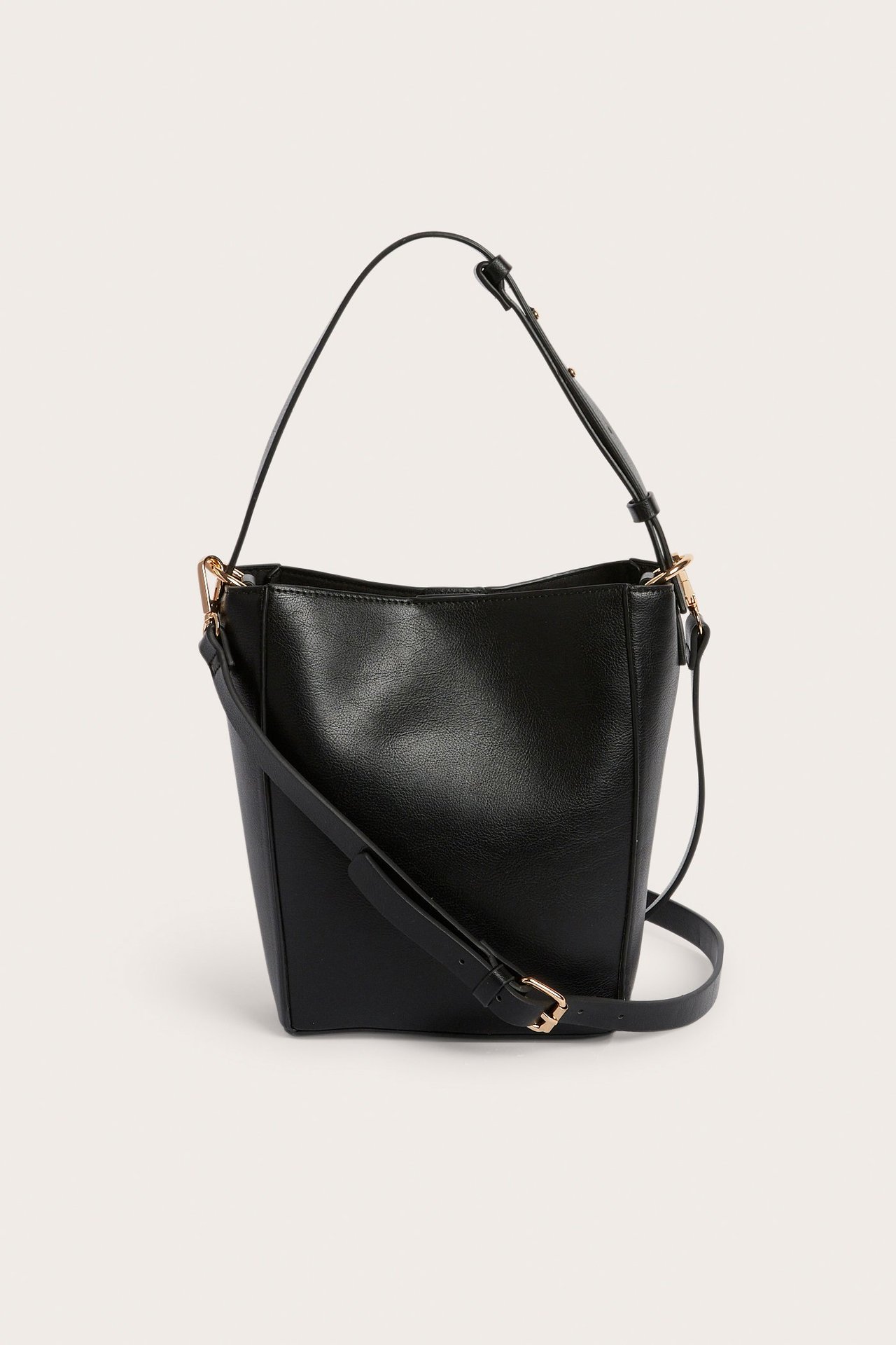 Frontvisning av svart bøtteveske i skinnimitasjon, med to justerbare stropper og gulldetaljer.