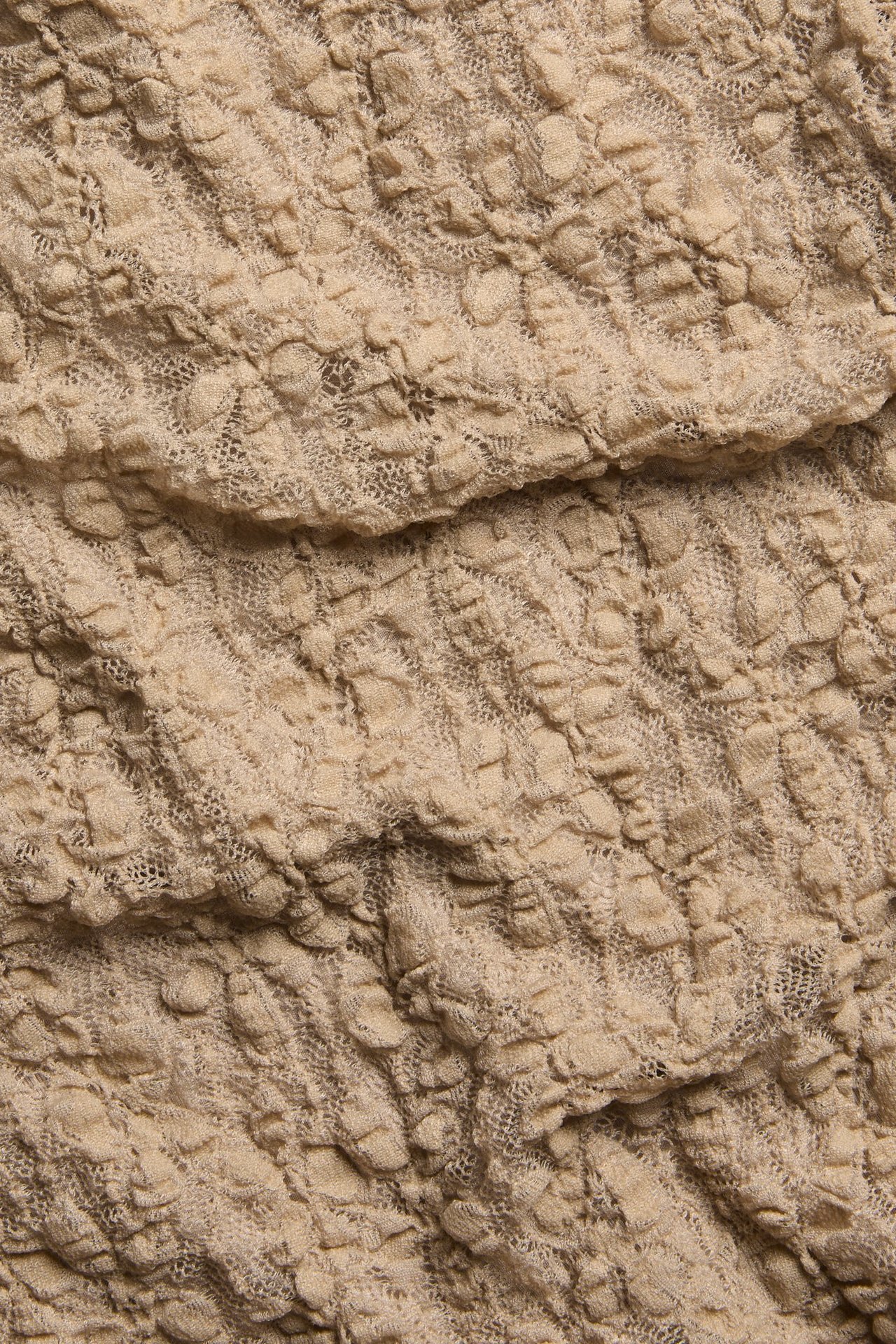 Zbliżenie beżowego topu z krótkim rękawem z teksturowanej koronki z wzorem na całej powierzchni.