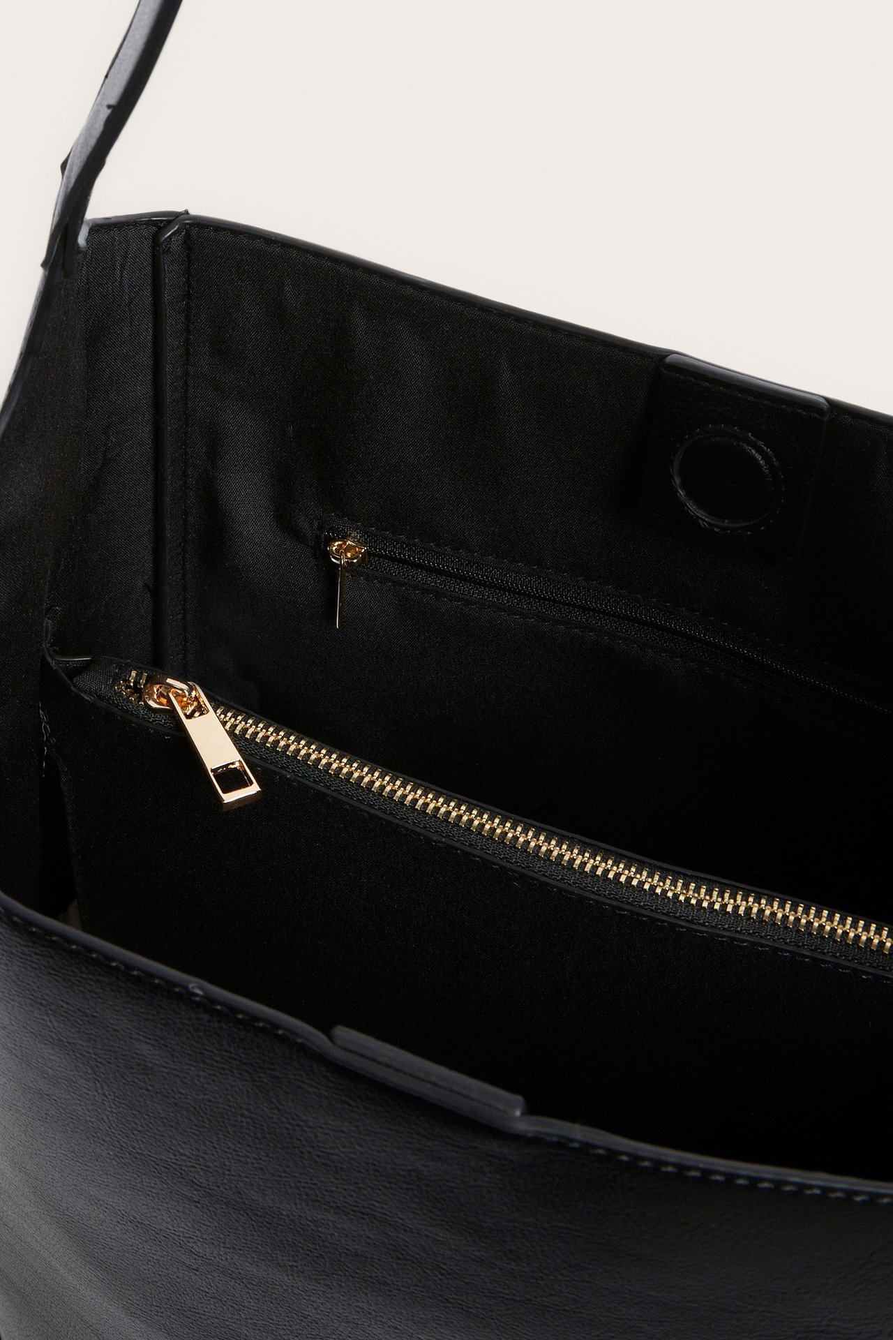 Lähikuva mustan PU-käsilaukun sisäosasta, jossa kultavetoketjullinen sisätasku ja magneettilukko.