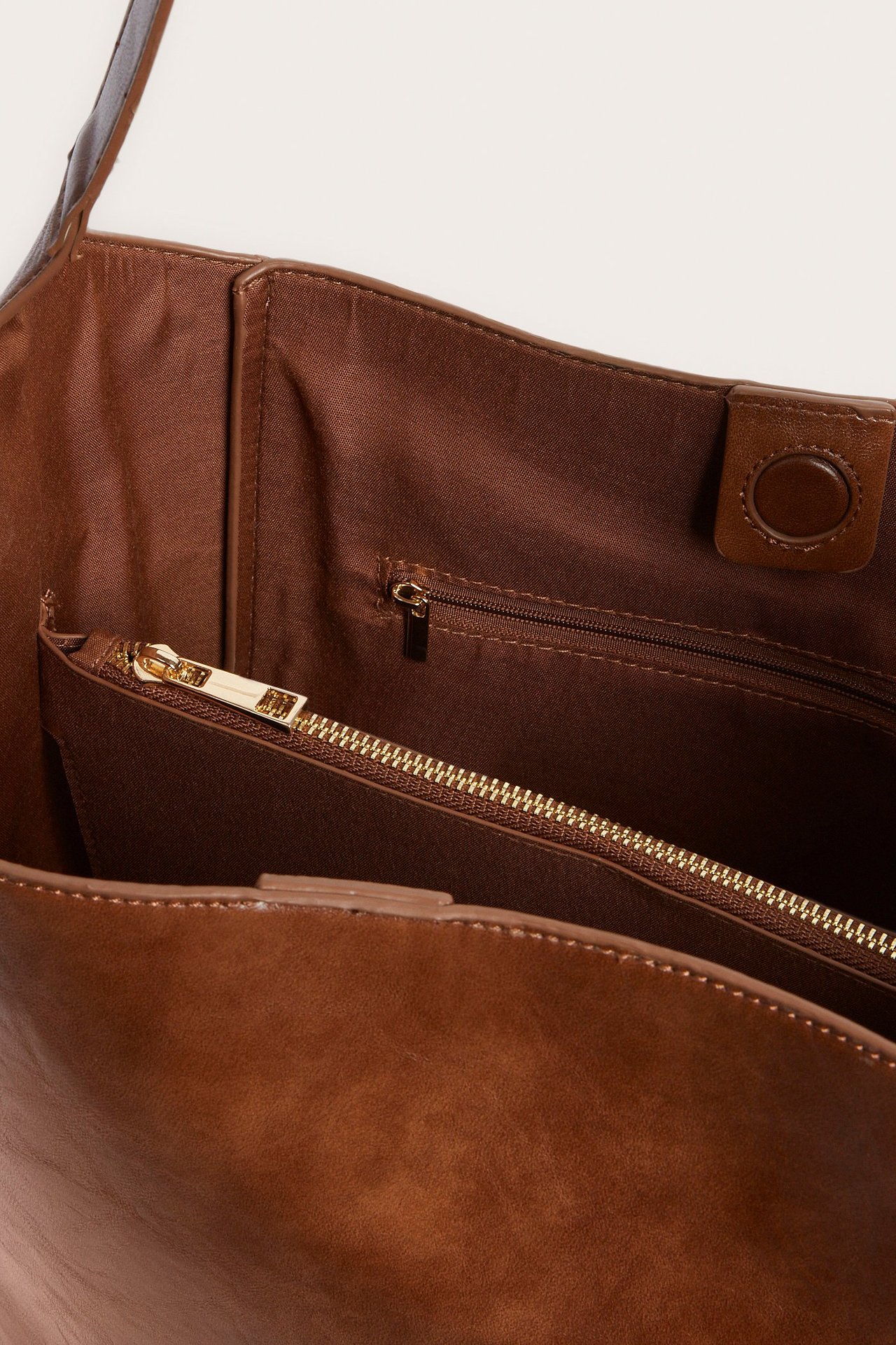 Lähikuva ruskean PU-käsilaukun sisäosasta, jossa magneettilukko ja vetoketjullinen sisätasku.