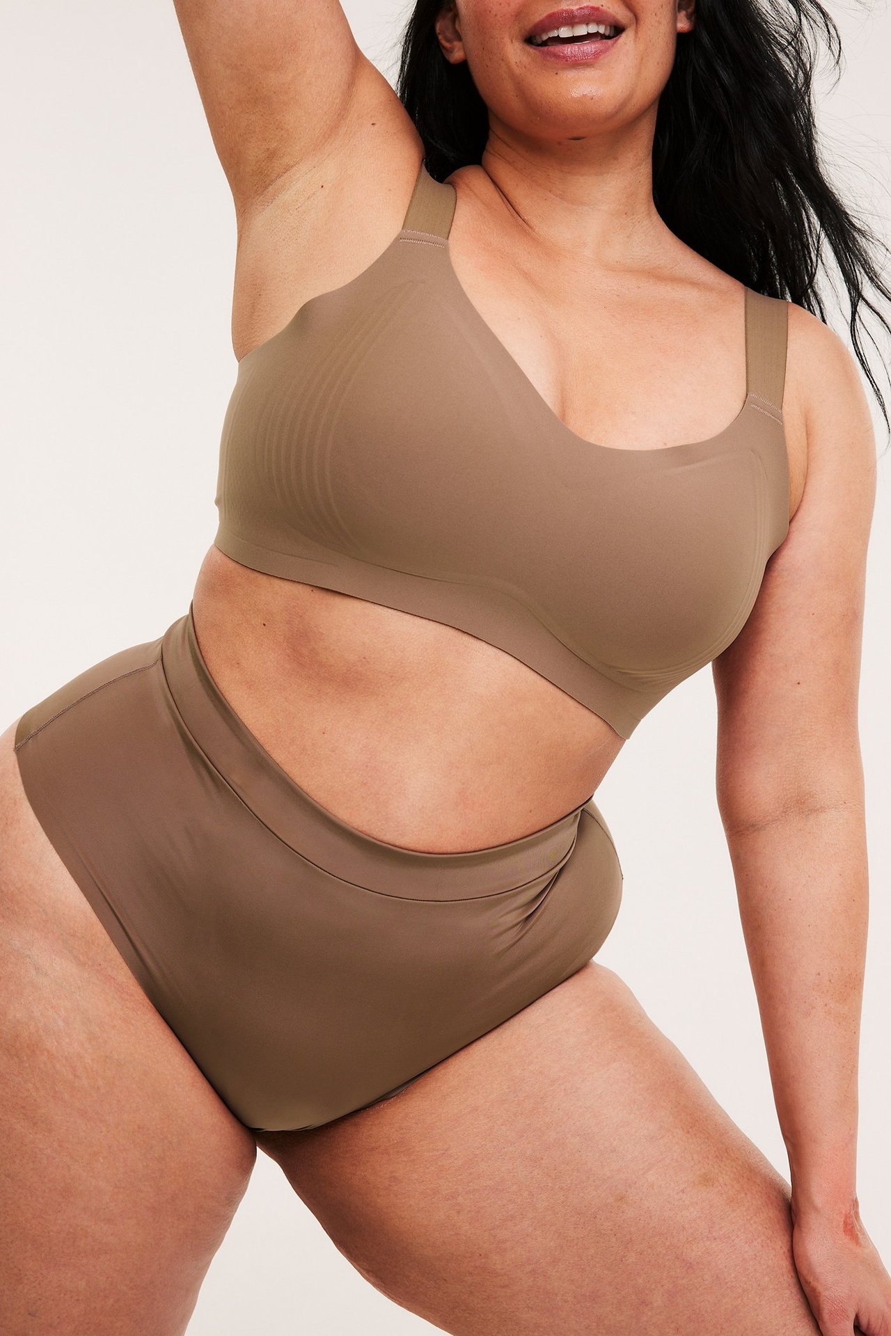 Edestäpäin nainen saumattomissa ruskeissa mikro-liiveissä ja niihin sopivissa korkeavyötäröisissä alushousuissa.