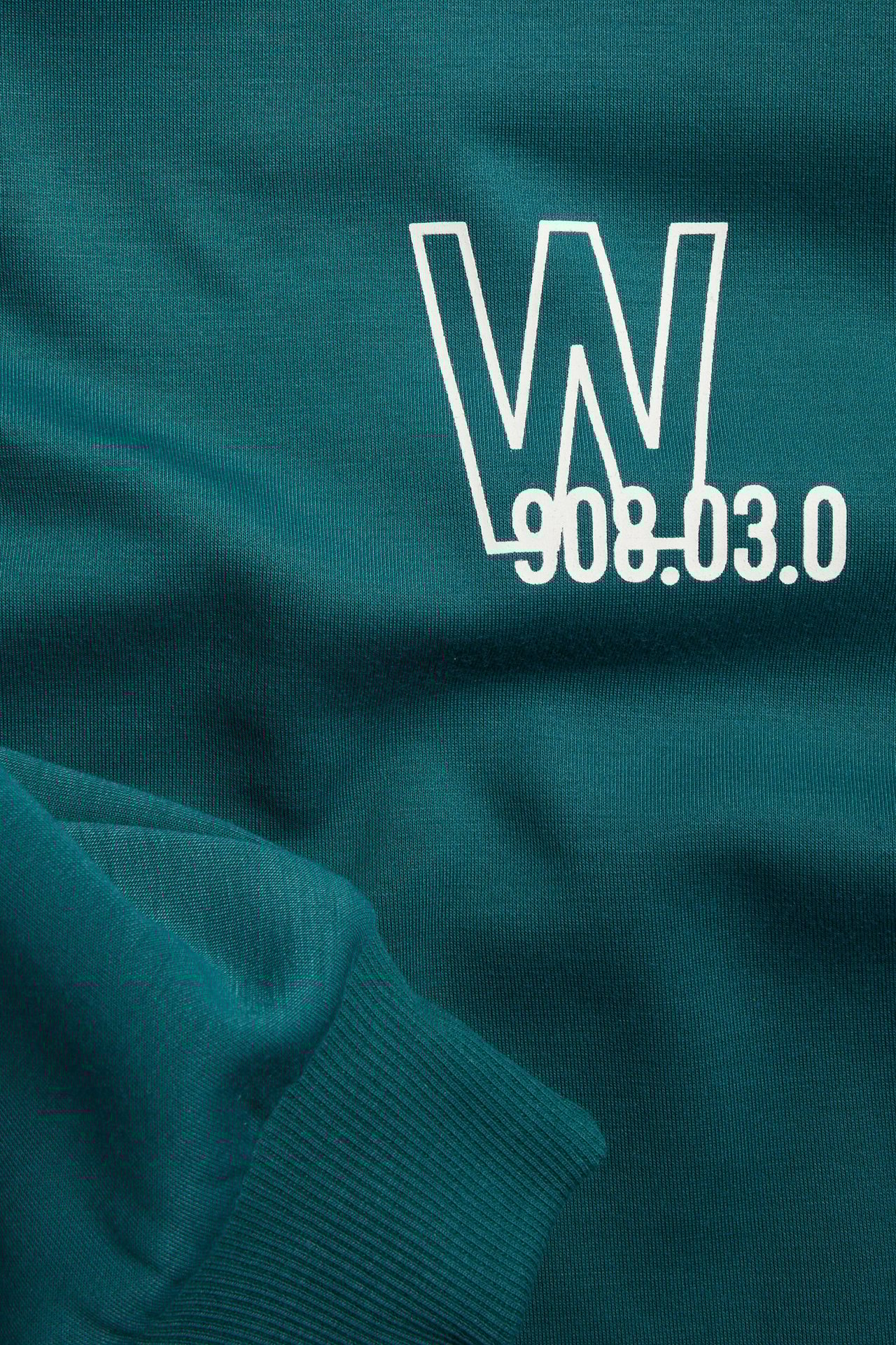 Zbliżenie z przodu: zielona bluza dresowa z tkaniny scuba, biały nadruk W i numerów, ściągacz.