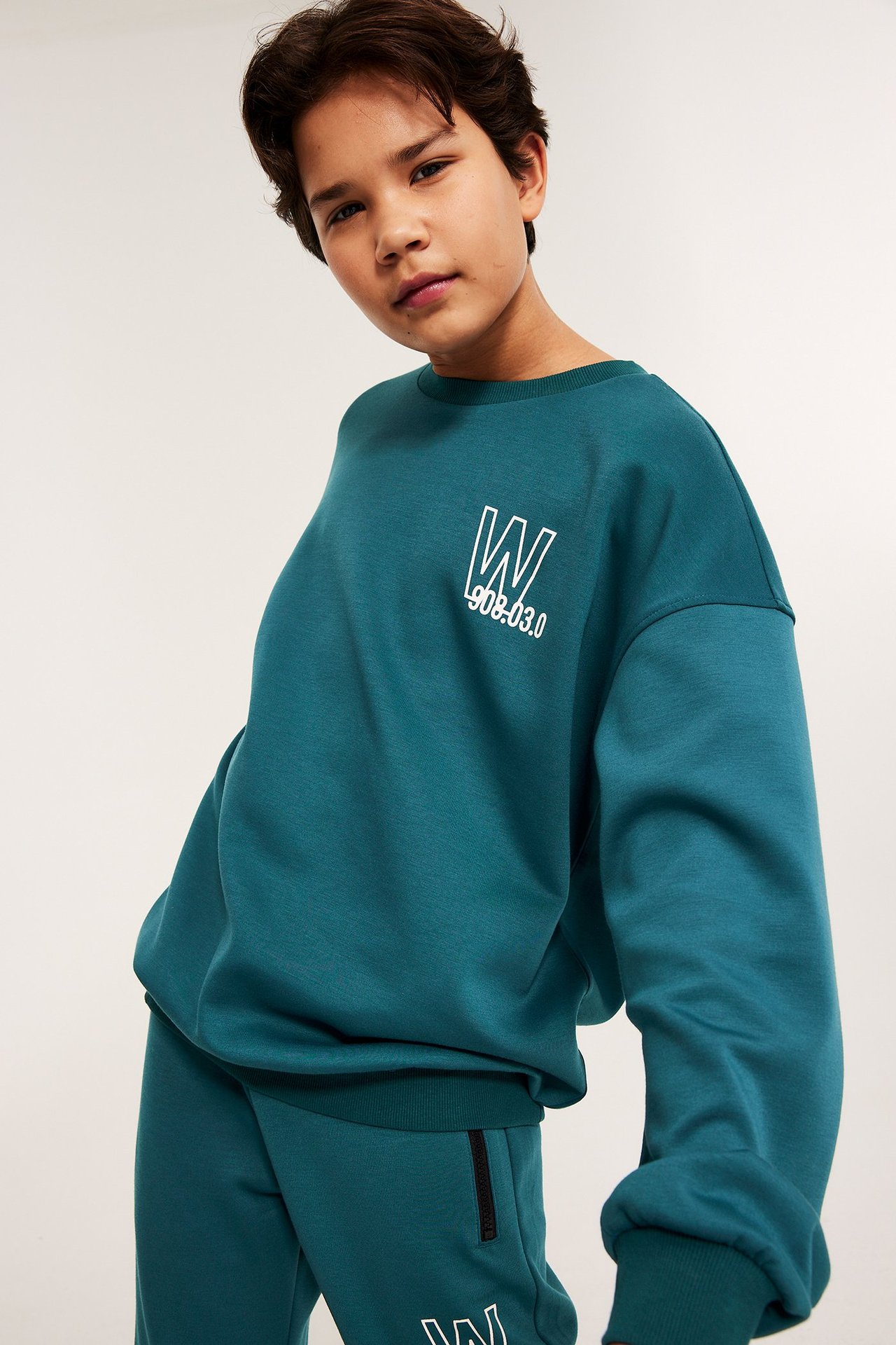 Forfra, barn i grønn sweatshirt i scubamateriale med hvitt trykk, og matchende joggebukse.