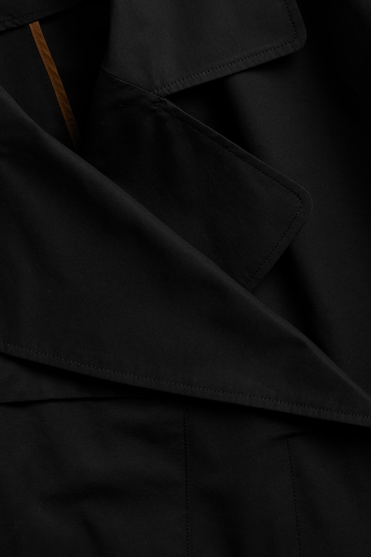 Närbild på svart trenchcoat i bomullsblandning, visar krage, slag och dekorativa sömmar.