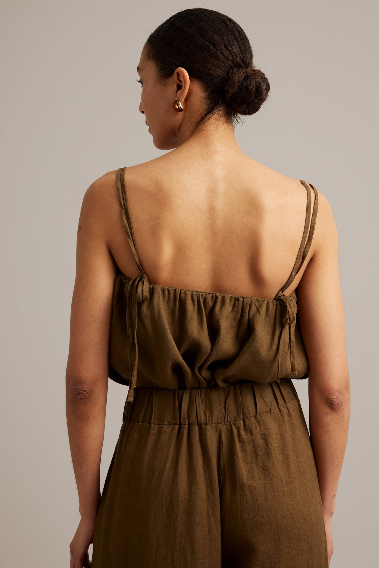 Ryggvy av kvinna i brunt linne med smala knutna axelband och matchande shorts.