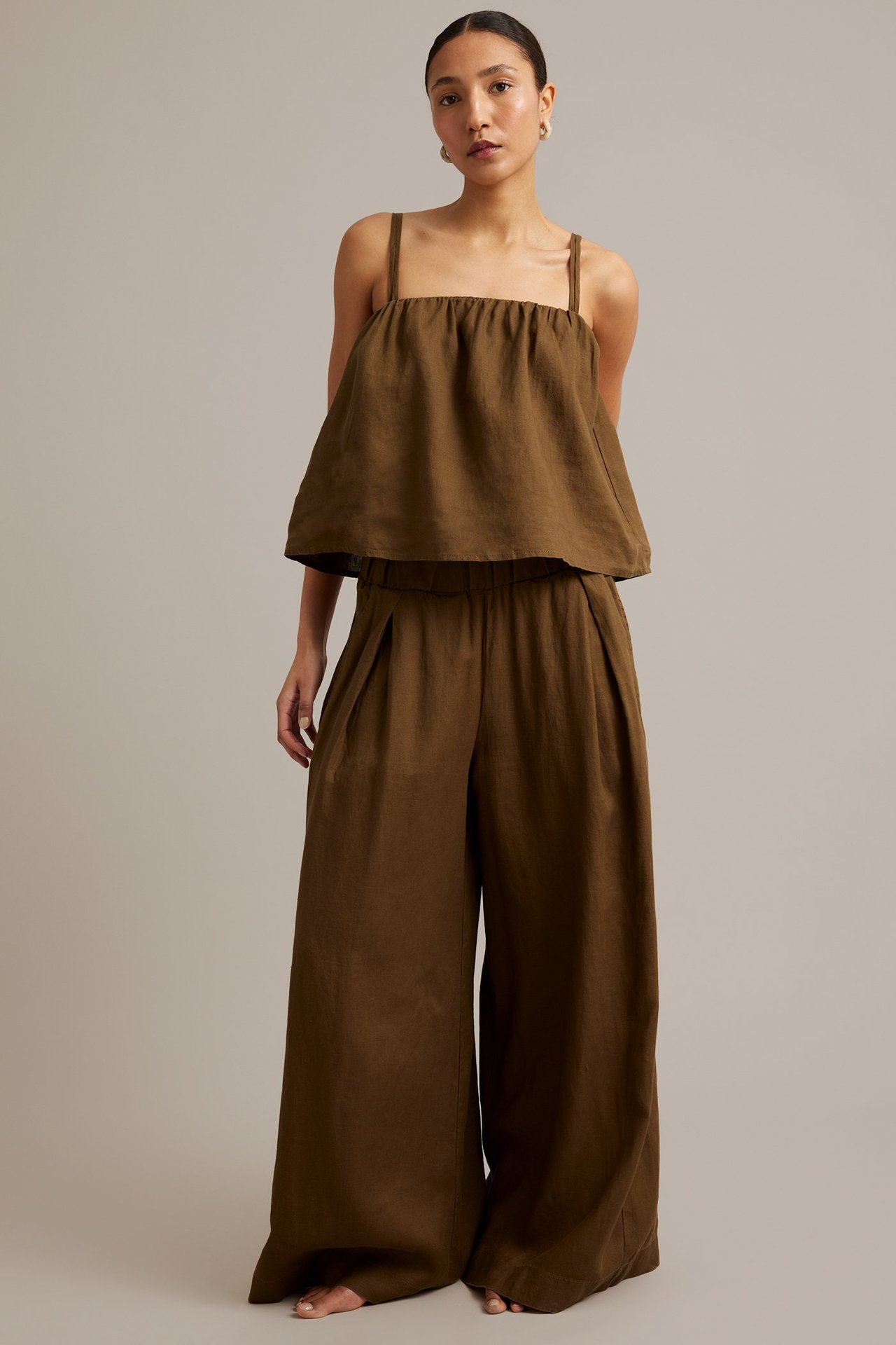 Frontvy: kvinna i brunt linne med smala axelband och matchande vida linnebyxor.