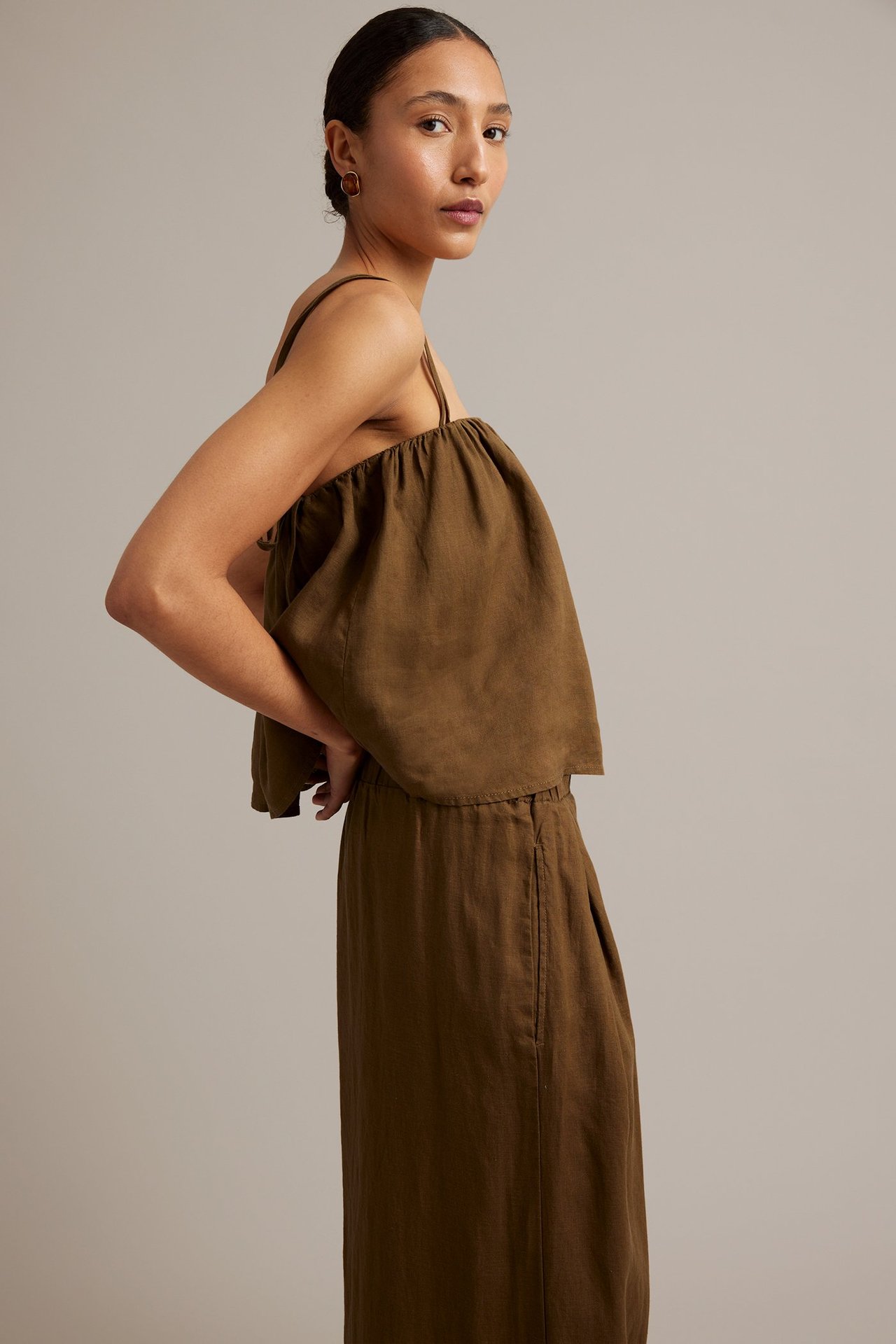 Sidovy av kvinna i brunt linne med smala axelband och matchande maxikjol i linne.