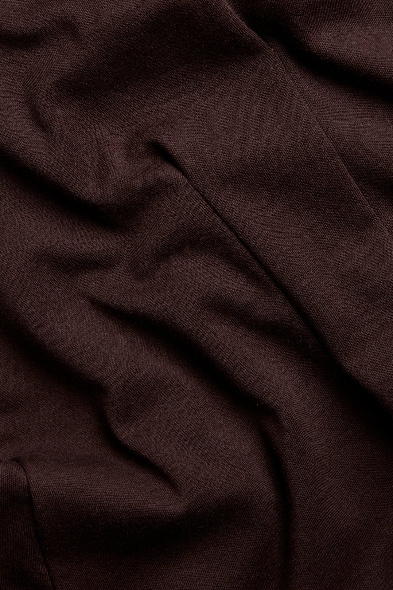 Zbliżenie na bordowy, jednolity materiał bawełniano-poliestrowy z miękkimi fałdami, część topu.