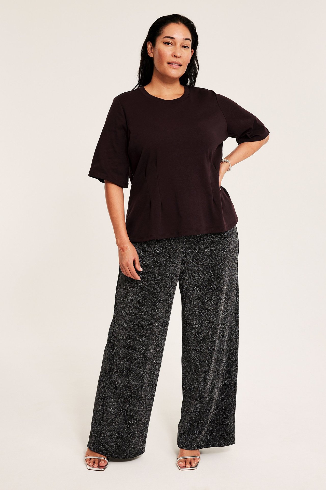 Kobieta w winie czerwonym dopasowanym topie z okrągłym dekoltem i szerokich czarnych spodni.