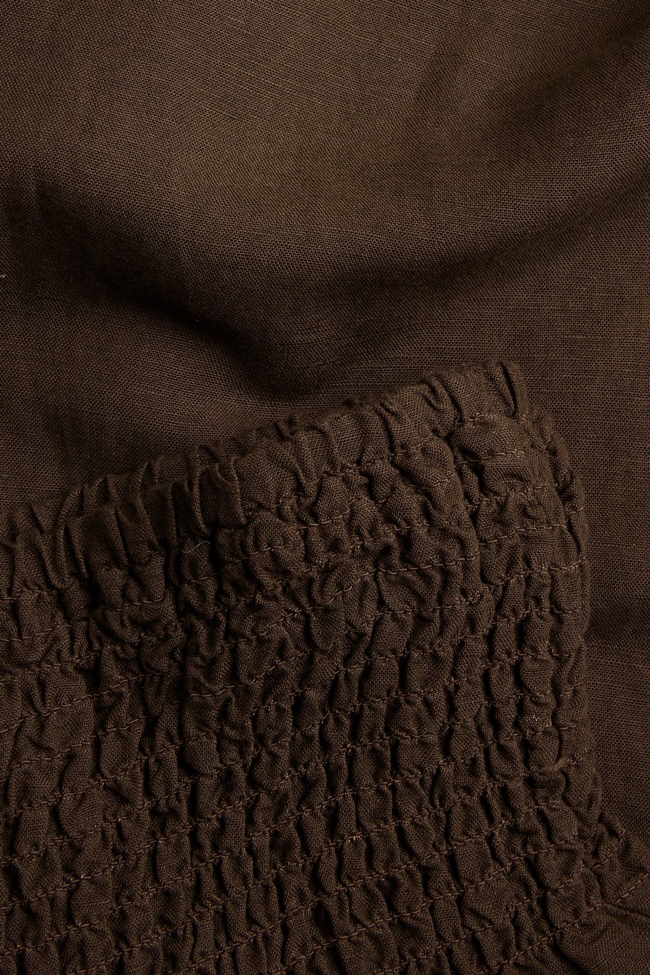 Nærbilde av mørkebrune vide linbuks med smock i midjen.