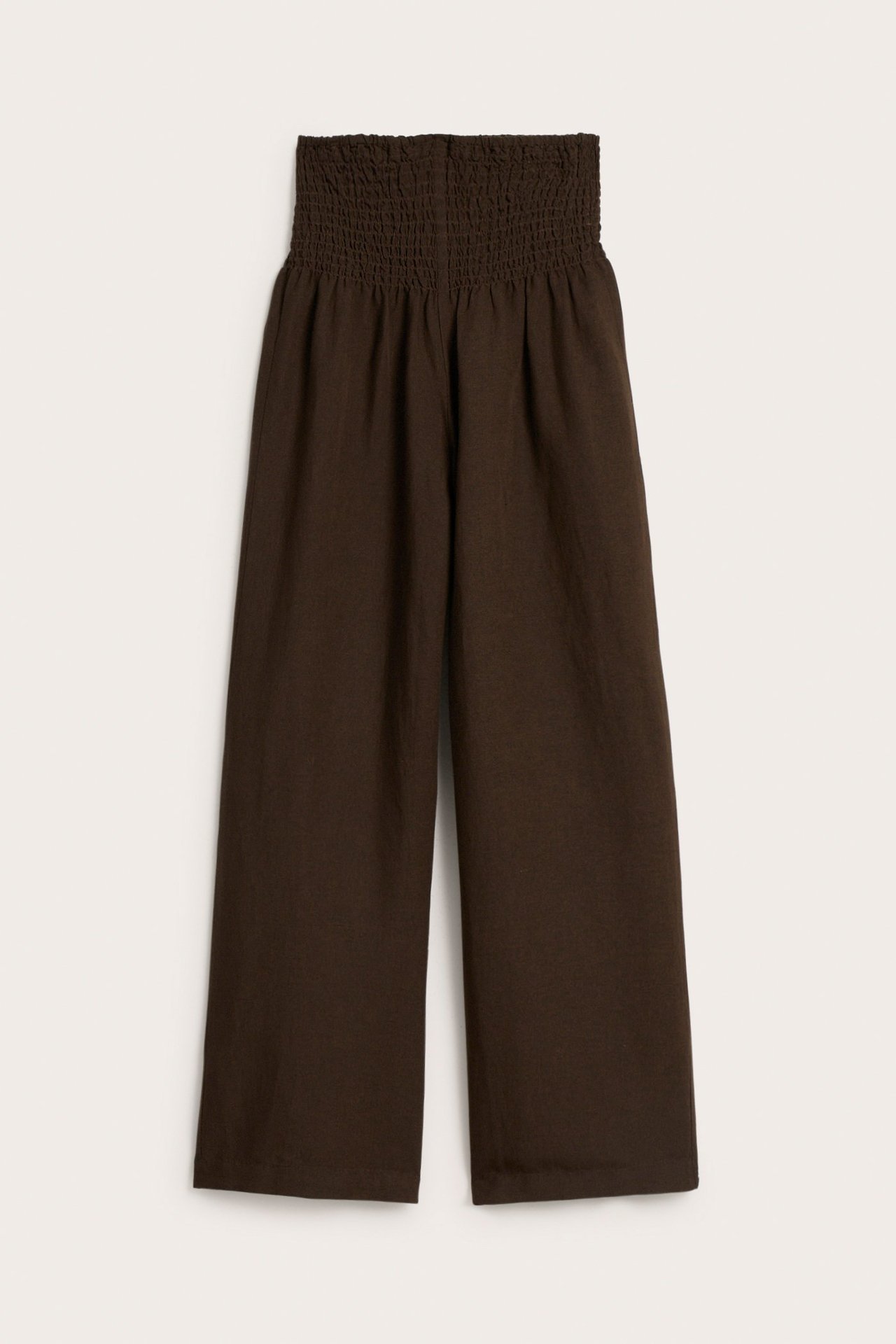 Frontbilde av mørkebrune vide linblandingsbukser med smock i midjen.