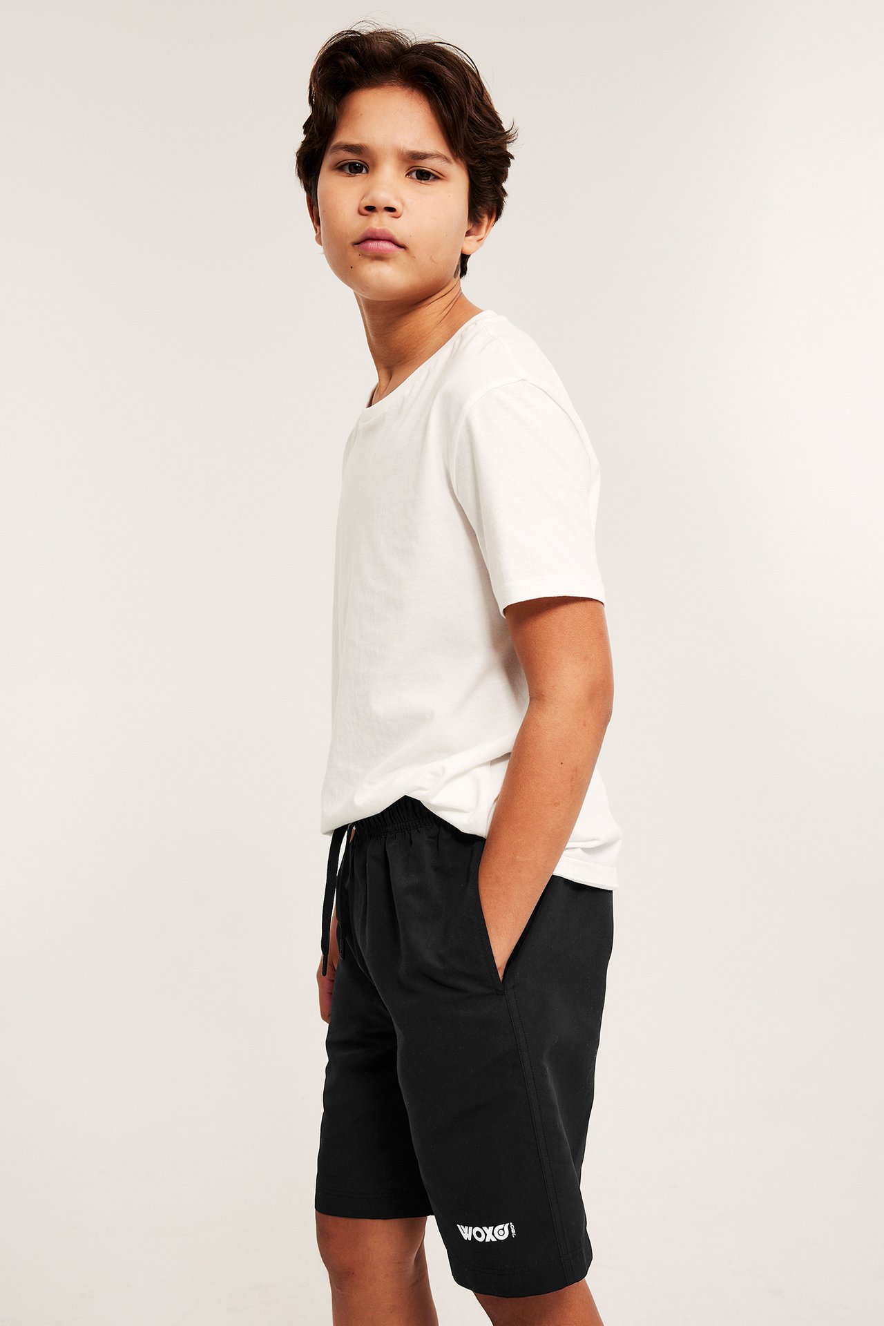 Sidovy av ett barn i svarta badshorts med dragsko i midjan och en vit t-shirt.