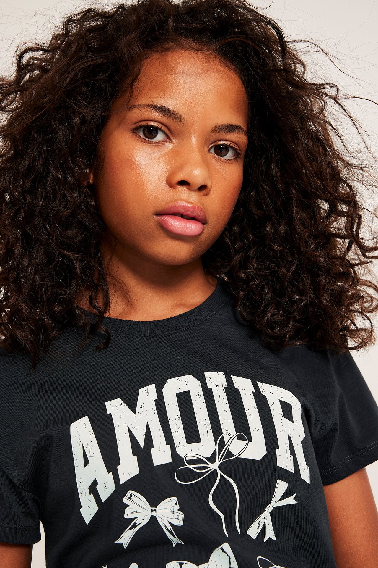 Närbild av ett barn i svart bomulls-t-shirt med vitt "AMOUR"-tryck och rosettmotiv.