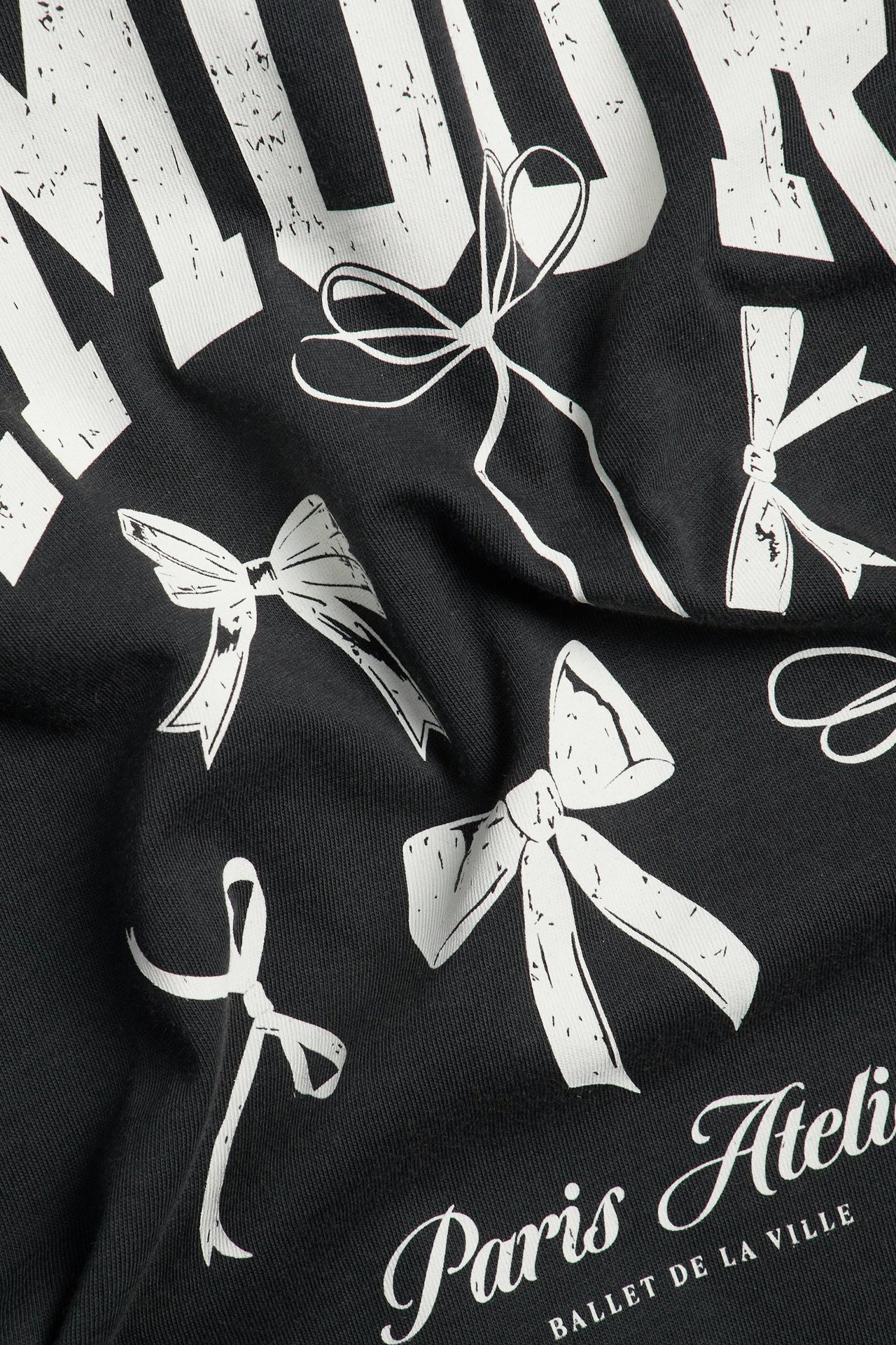 Närbild av en svart bomulls-t-shirt med slitet vitt tryck av rosetter och text.