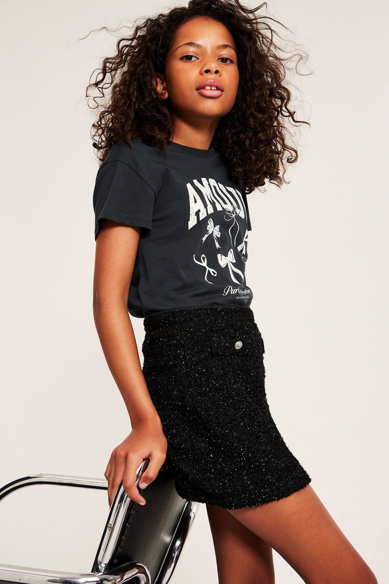 Frontvy: Kid bär en svart bomulls-t-shirt med vitt tryck och en svart tweedkjol.