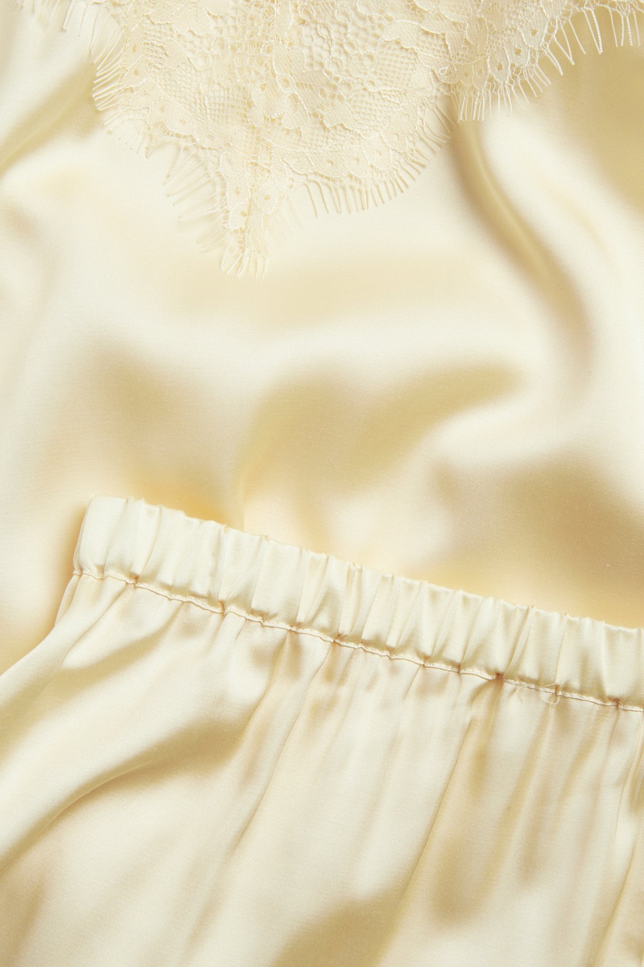 Närbild på ljusgul satinpyjamas med spetsdetalj på toppen och shorts med resår.