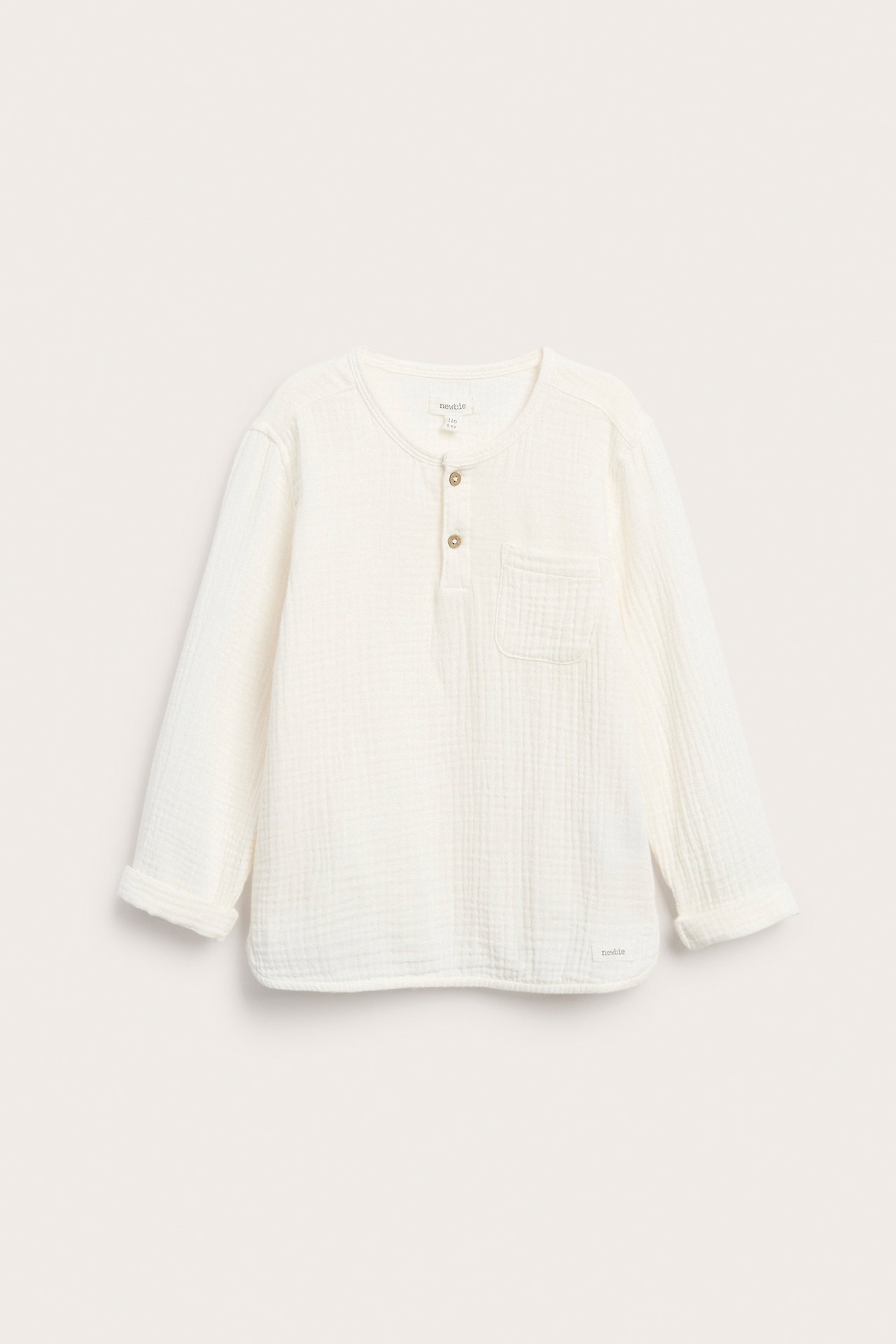 Edestä kuvattu luonnonvalkoinen pitkähihainen puuvillamusliinipaita, jossa nappilista, rintatasku ja käärityt hihat.