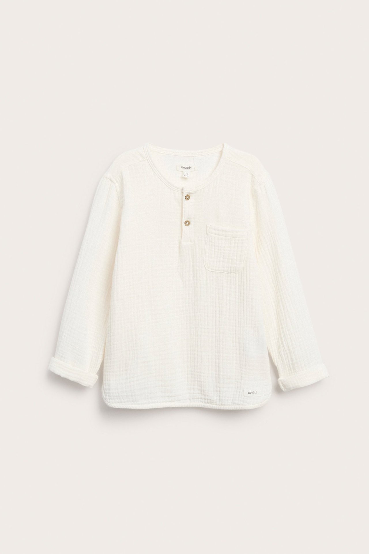 Frontvisning av en offwhite langermet bomullsmuslin-topp med knappestolpe, brystlomme og opprullede ermer.