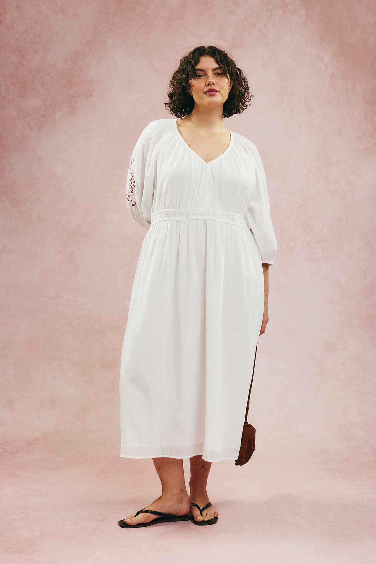 Widok z przodu: kobieta w białej bawełnianej sukience, haftowane rękawy, czarne japonki, brązowa torebka.