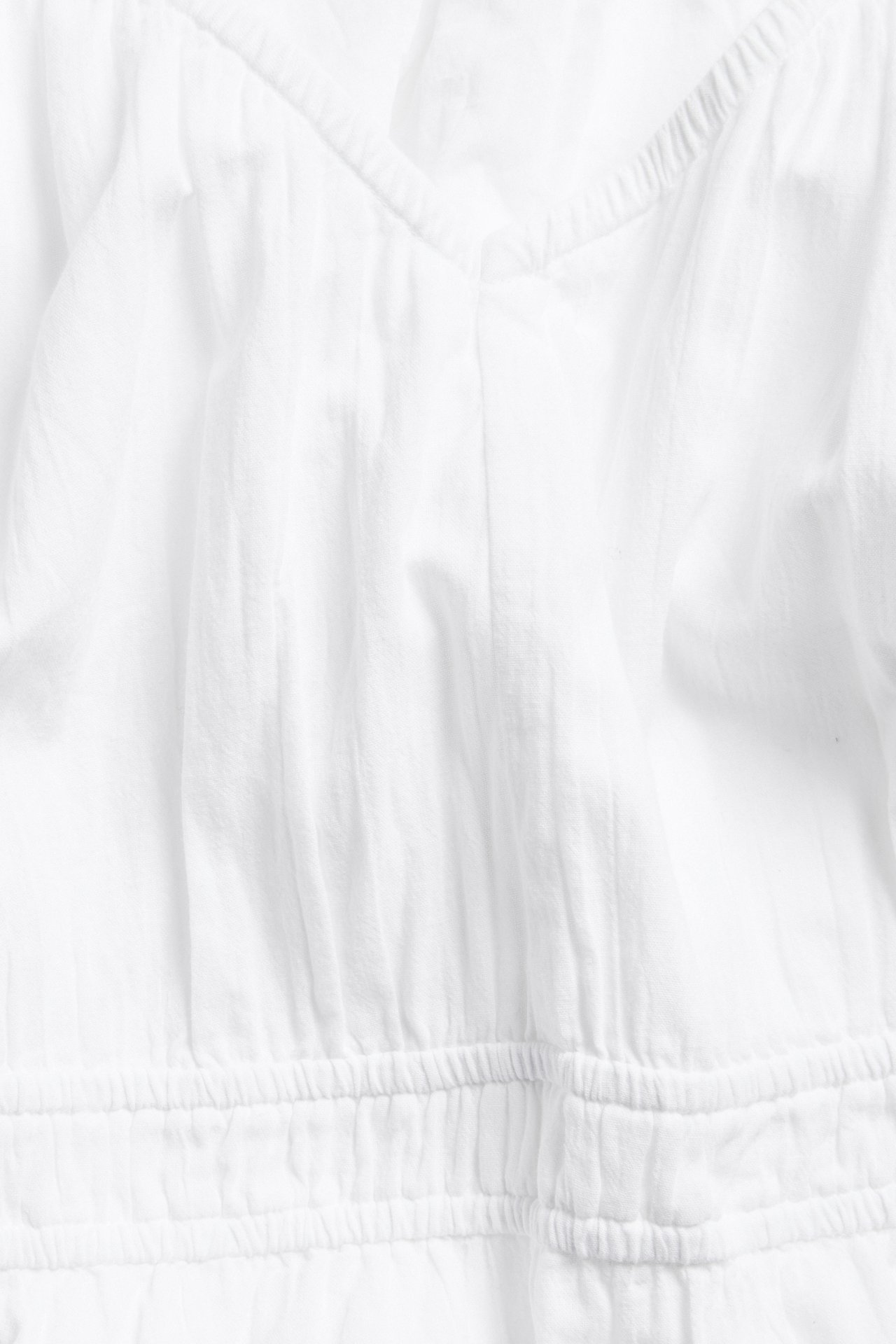 Lähikuva valkoisesta puuvillamekosta, jossa V-pääntie ja joustava vyötärö.