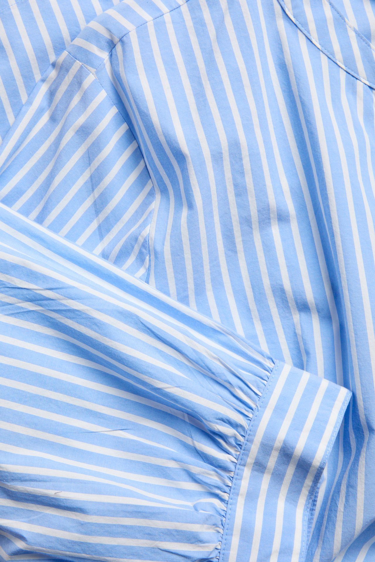 Närbild av en blå- och vitrandig poplinklänning i bomull, visar en rynkad 3/4-ärm.