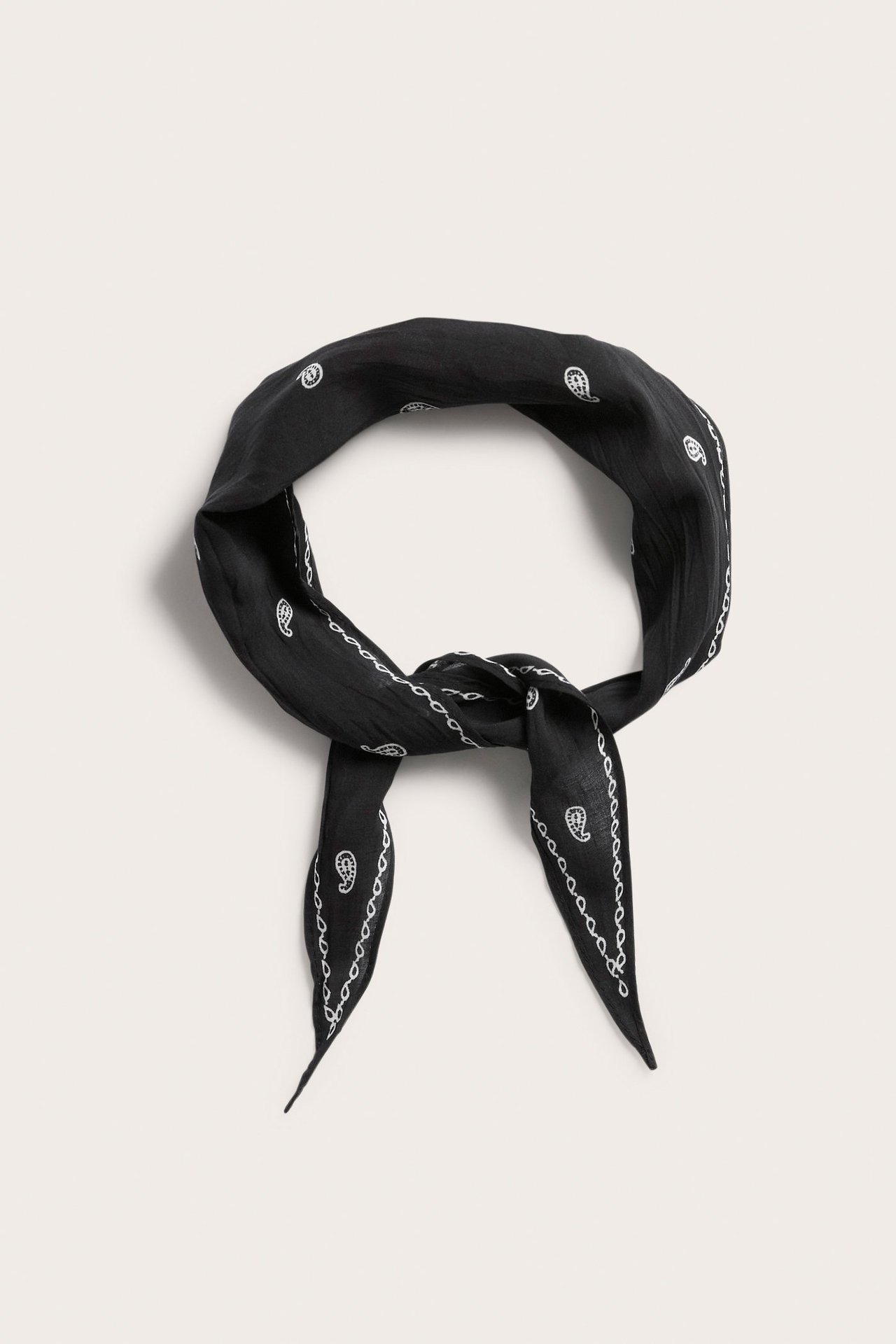 Edestä näkymä mustasta rypistetystä huivista, jossa valkoinen paisleymäinen kuvio, solmittuna solmulla.