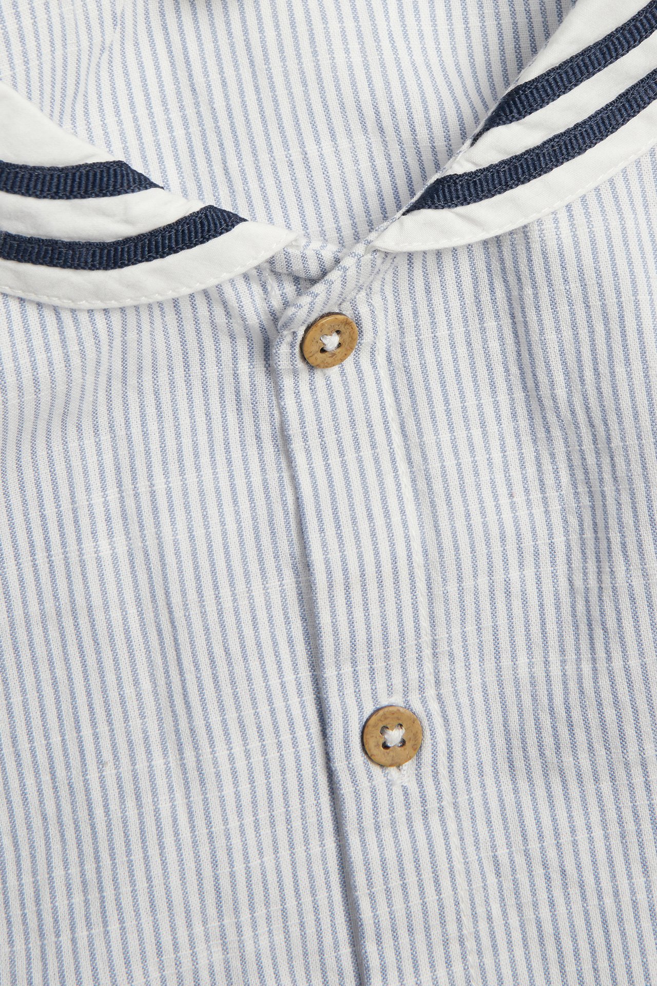 Zbliżenie przodem: niebiesko-biała koszula bawełniana w paski, z marynarskim kołnierzem i drewnianymi guzikami.