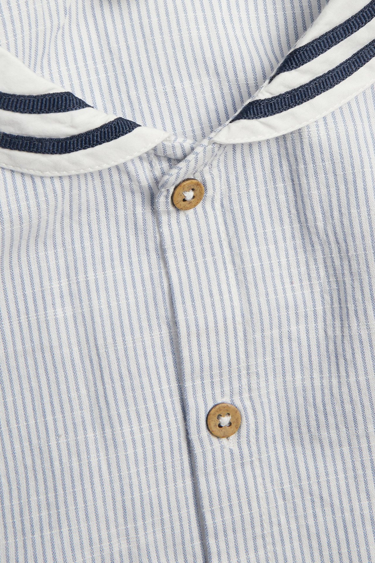 Zbliżenie przodem: niebiesko-biała koszula bawełniana w paski, z marynarskim kołnierzem i drewnianymi guzikami.