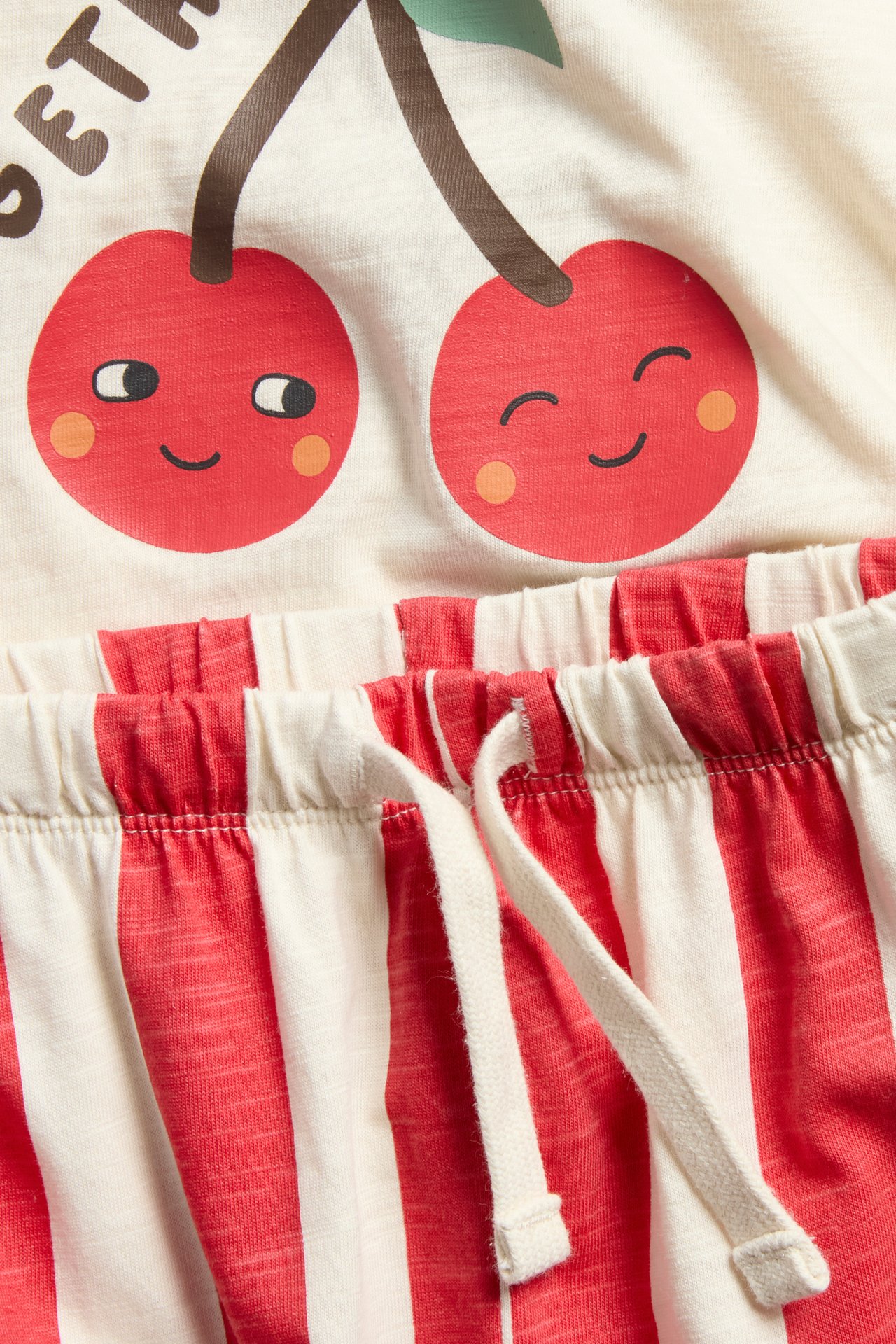 Lähikuva vauvan punaisesta ja kermanvärisestä puuvillasarjasta: kirsikkakuvioinen T-paita ja raidalliset collegehousut.