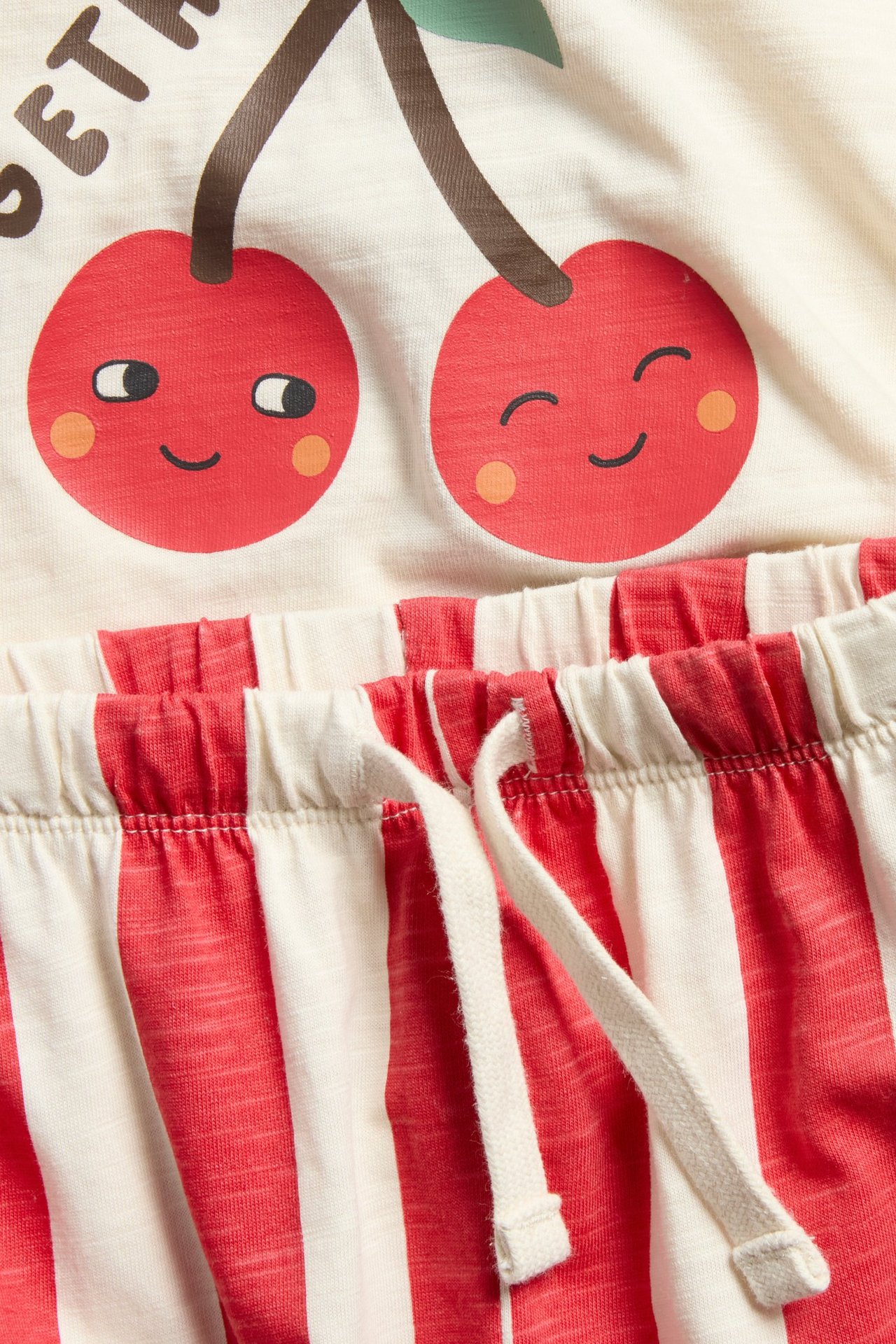 Zbliżenie na bawełniany komplet niemowlęcy w czerwono-kremowe paski: koszulka z wiśniami i spodnie dresowe.