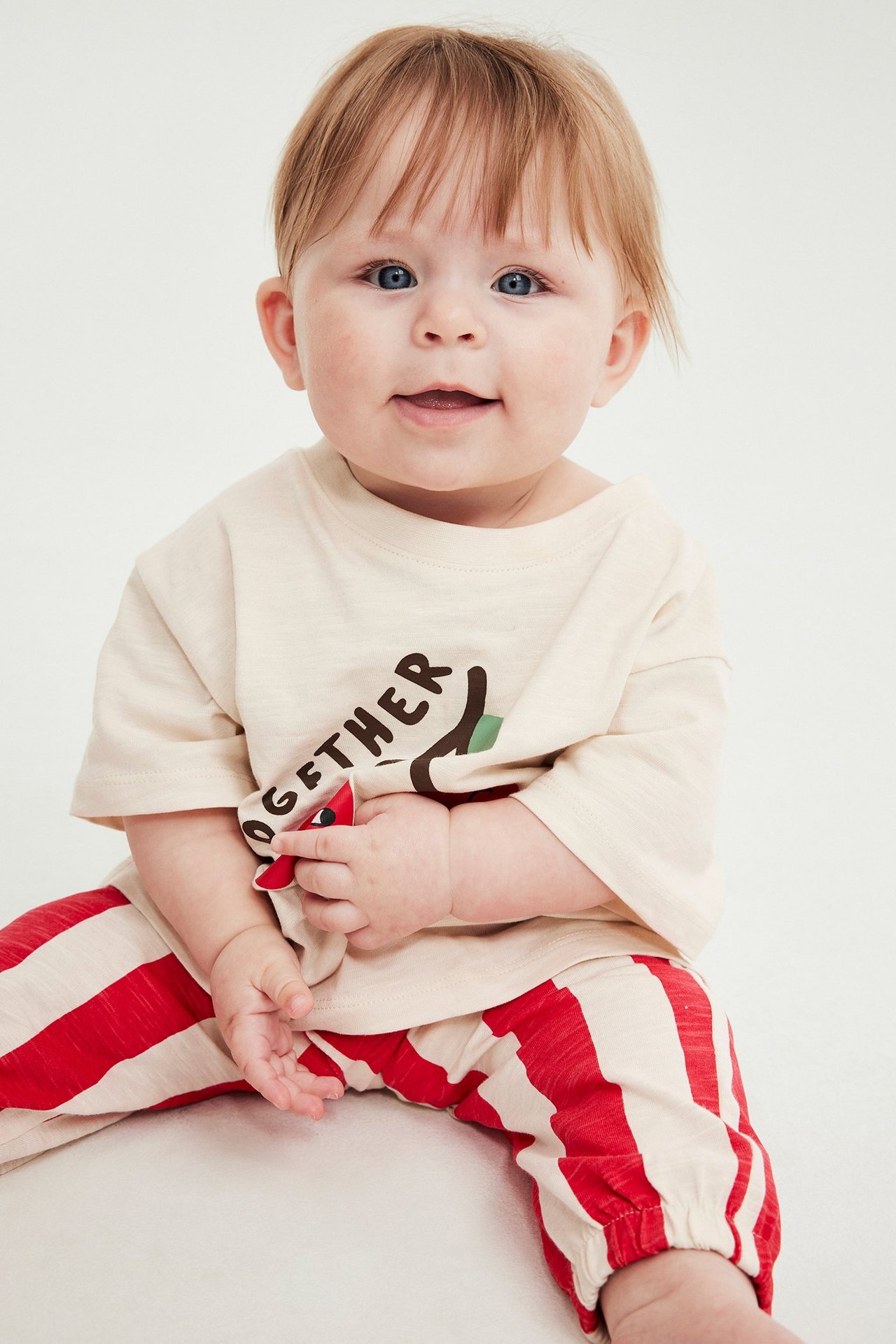 Widok z przodu dziecka w beżowej koszulce z nadrukiem i czerwono-beżowych spodniach dresowych w paski.