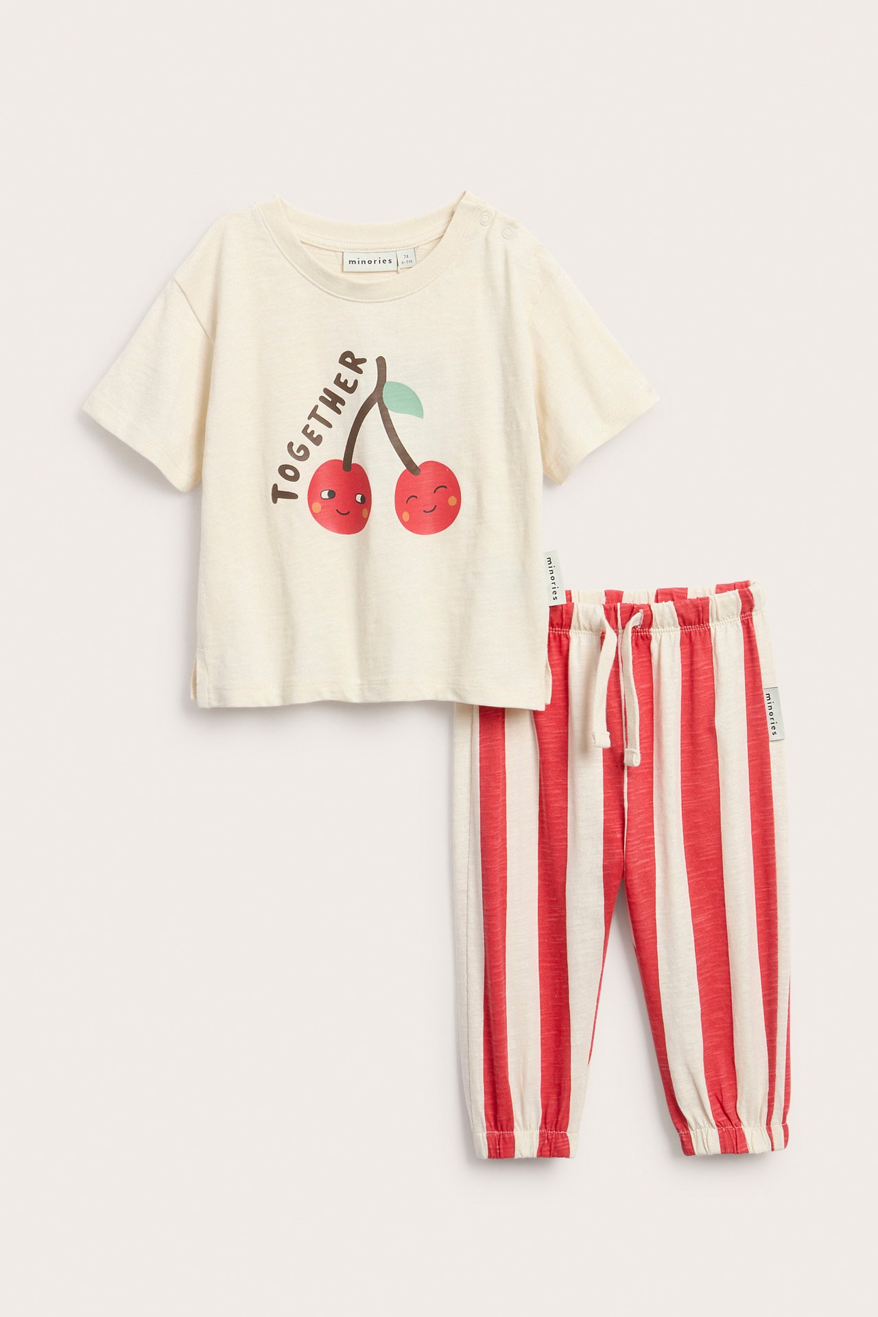 Edestä: Vauvan luonnonvalkoinen T-paita kirsikkapainatuksella. Punaraidalliset puuvillajogginghousut.