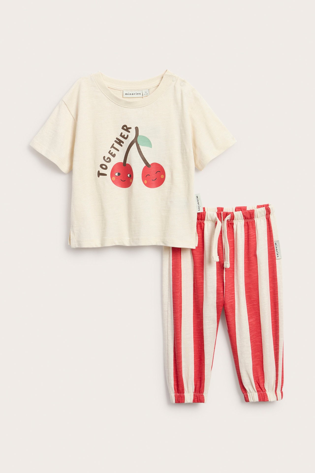Widok z przodu: Kremowy T-shirt niemowlęcy z nadrukiem wiśni, napami i czerwone dresowe spodnie w paski ze sznurkiem.