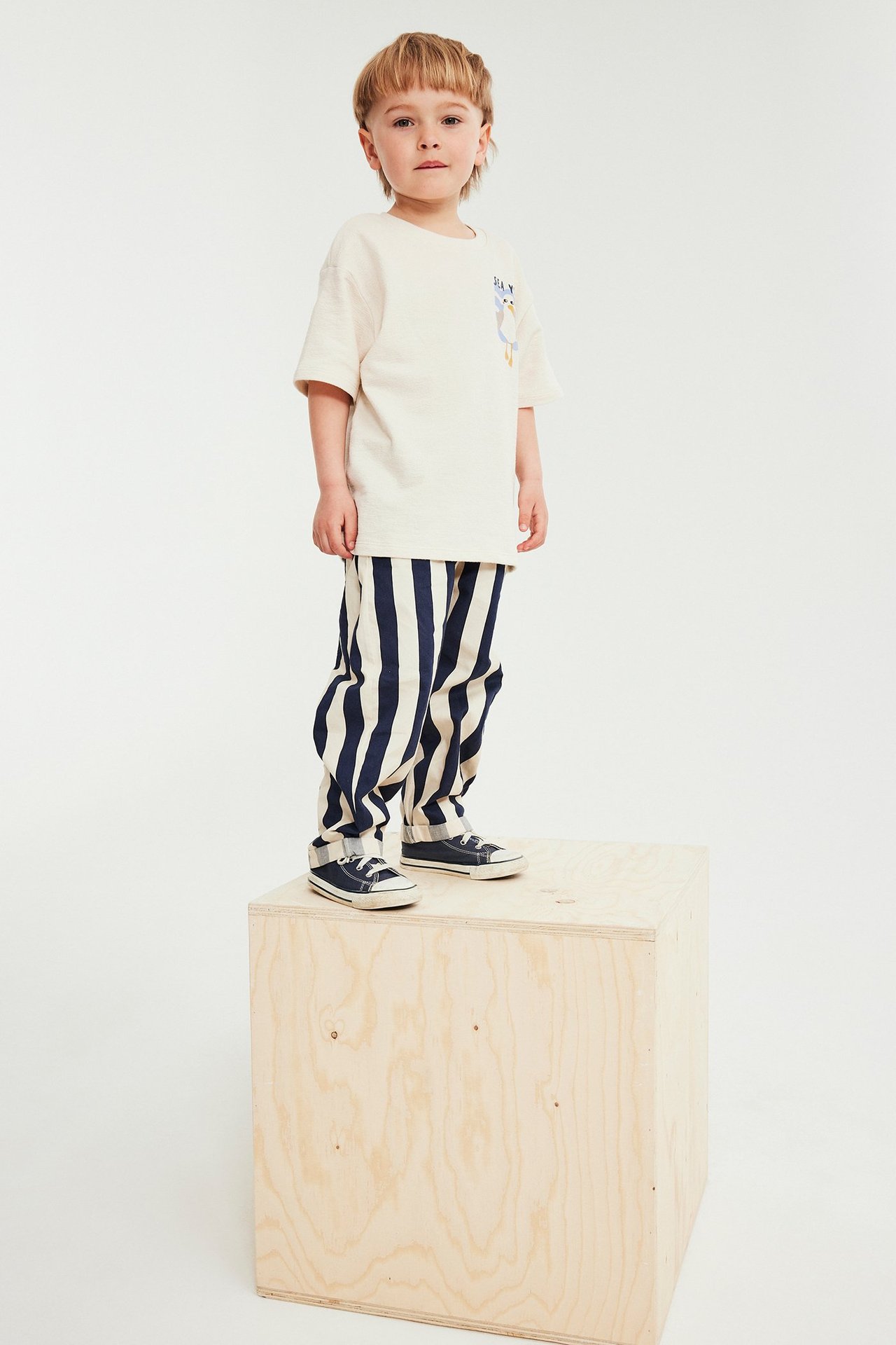 Frontvisning, barn i lys beige bomulls-t-skjorte med dyretrykk, stripete bukser og joggesko.