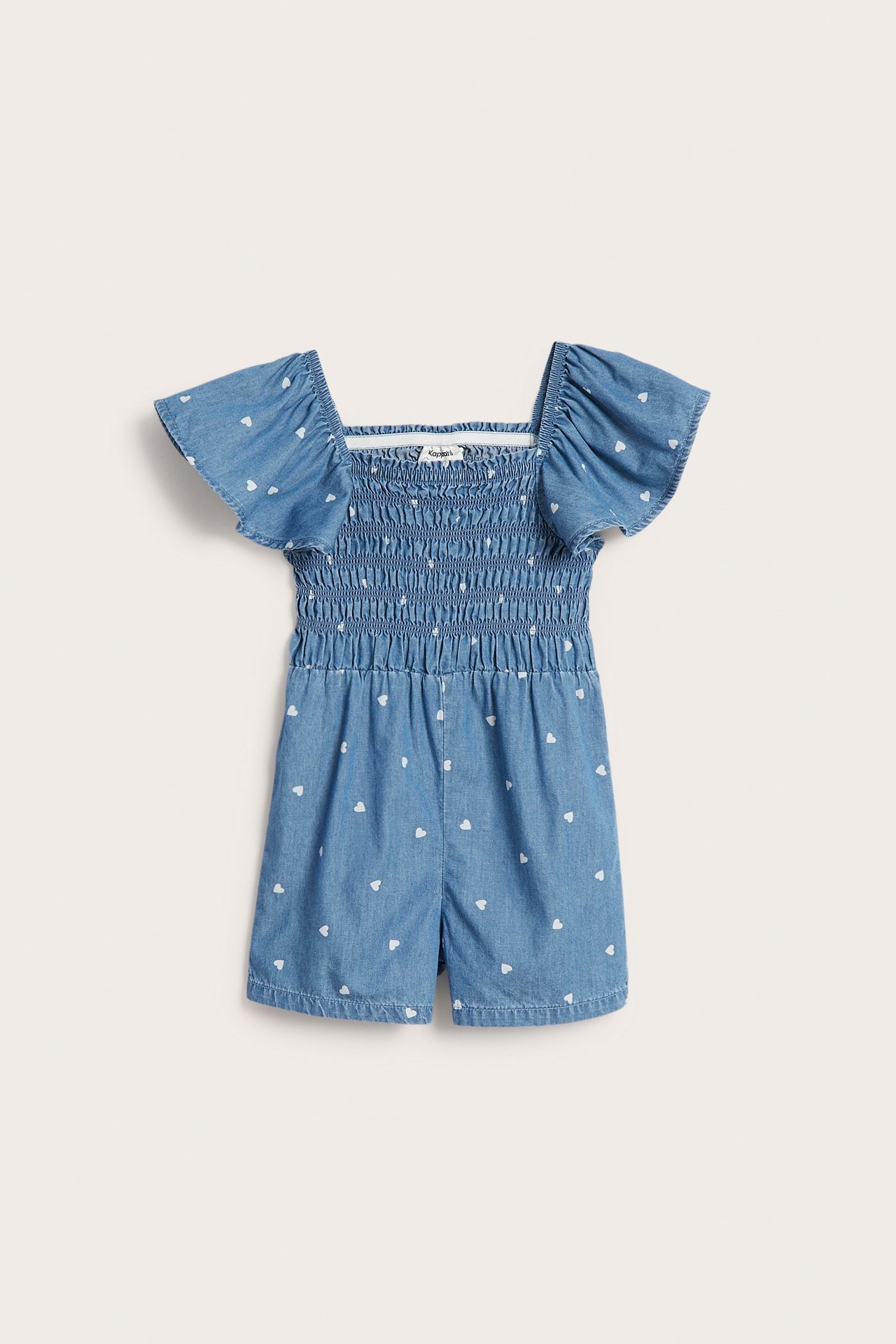 Frontvisning av en lys blå denim playsuit for barn med hvitt hjerteprint, smock og volangermer.