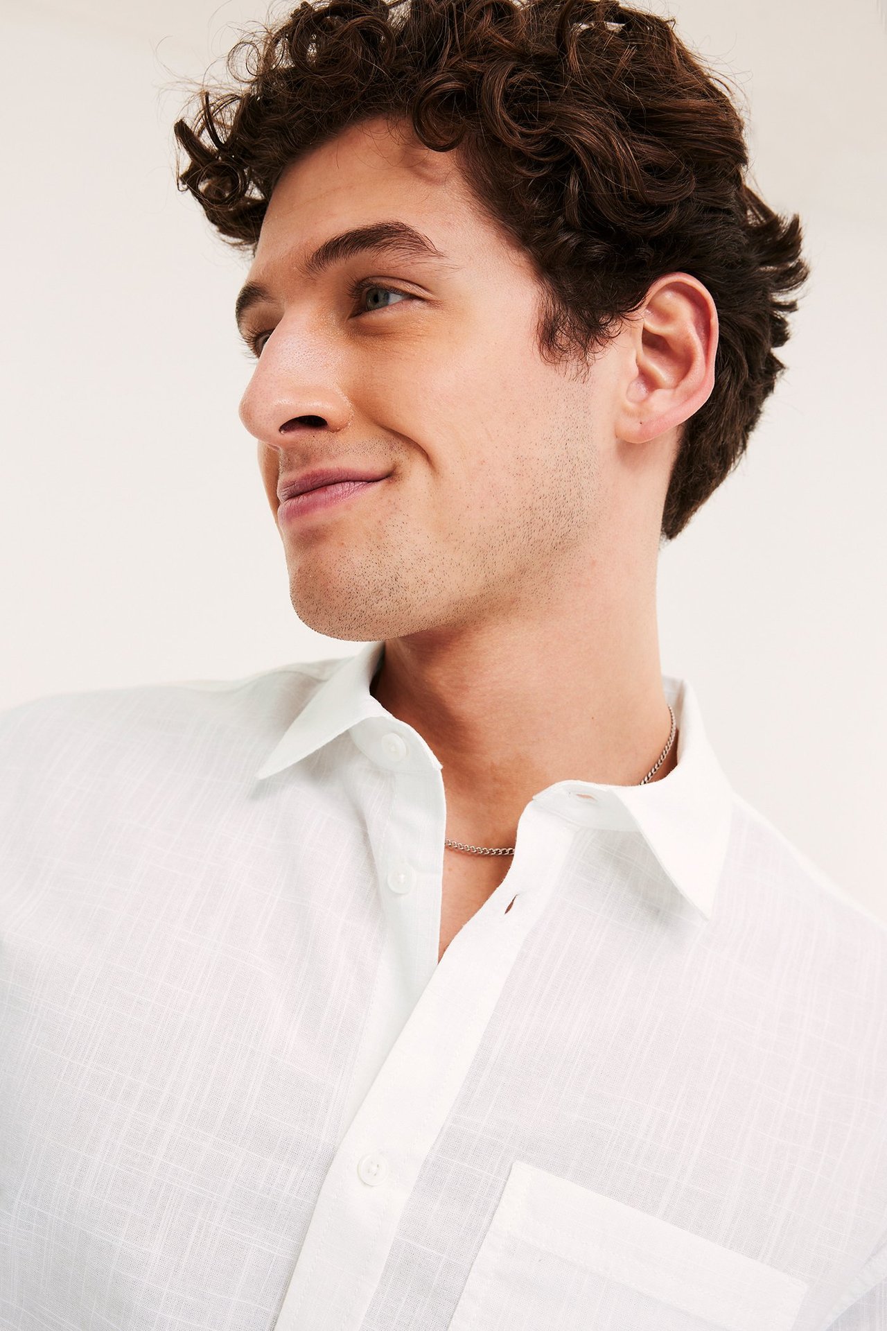 Zbliżenie mężczyzny w białej, strukturalnej koszuli z krótkim rękawem, kieszenią i srebrnym łańcuszkiem.