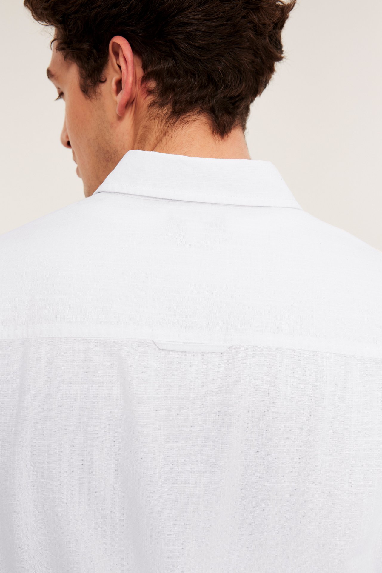 Lähikuva takaapäin miehestä, yllään valkoinen lyhythihainen regular fit -paita rakennekuviolla.