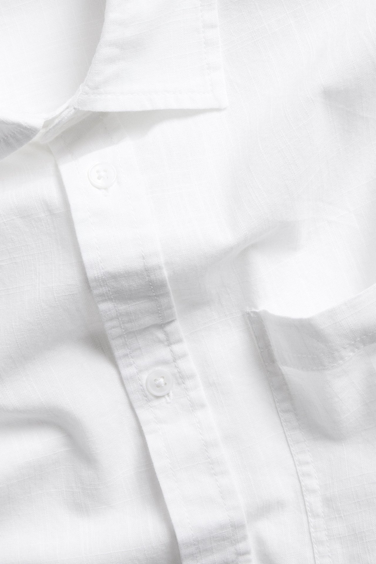 Zbliżenie białej koszuli z krótkim rękawem, o teksturowanej tkaninie, normalnym kołnierzyku, kieszonce na piersi i guzikach.