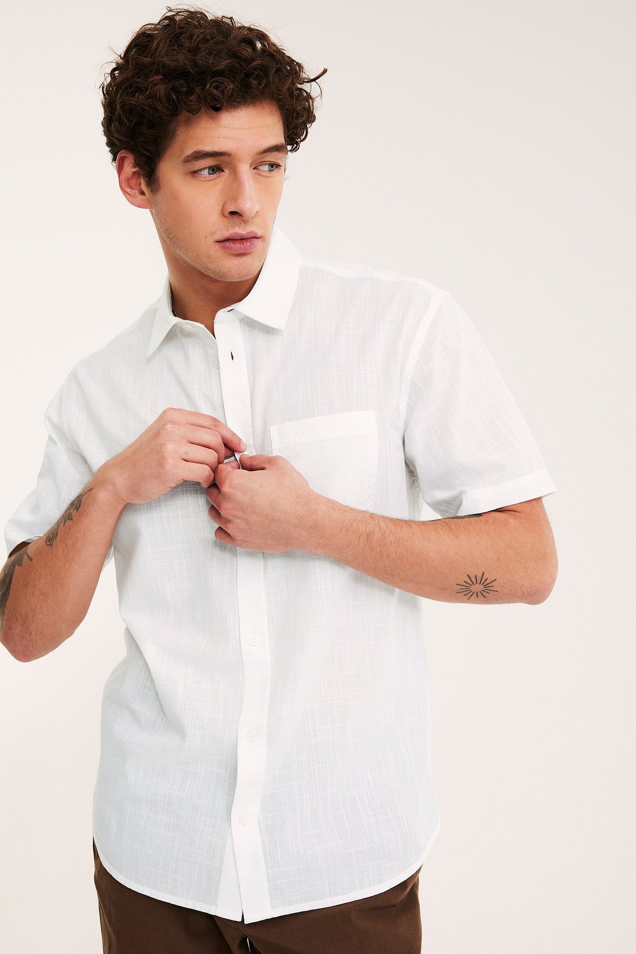 Forfra: mann knepper hvit teksturert kortermet regular fit skjorte med brystlomme, brune bukser.